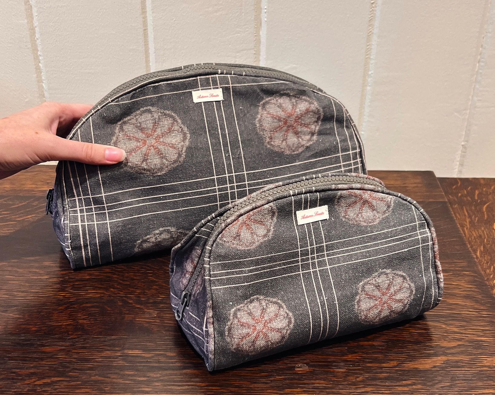 a hand picking up the Autumn Sonata Eva toiletry bag with the small infront of it