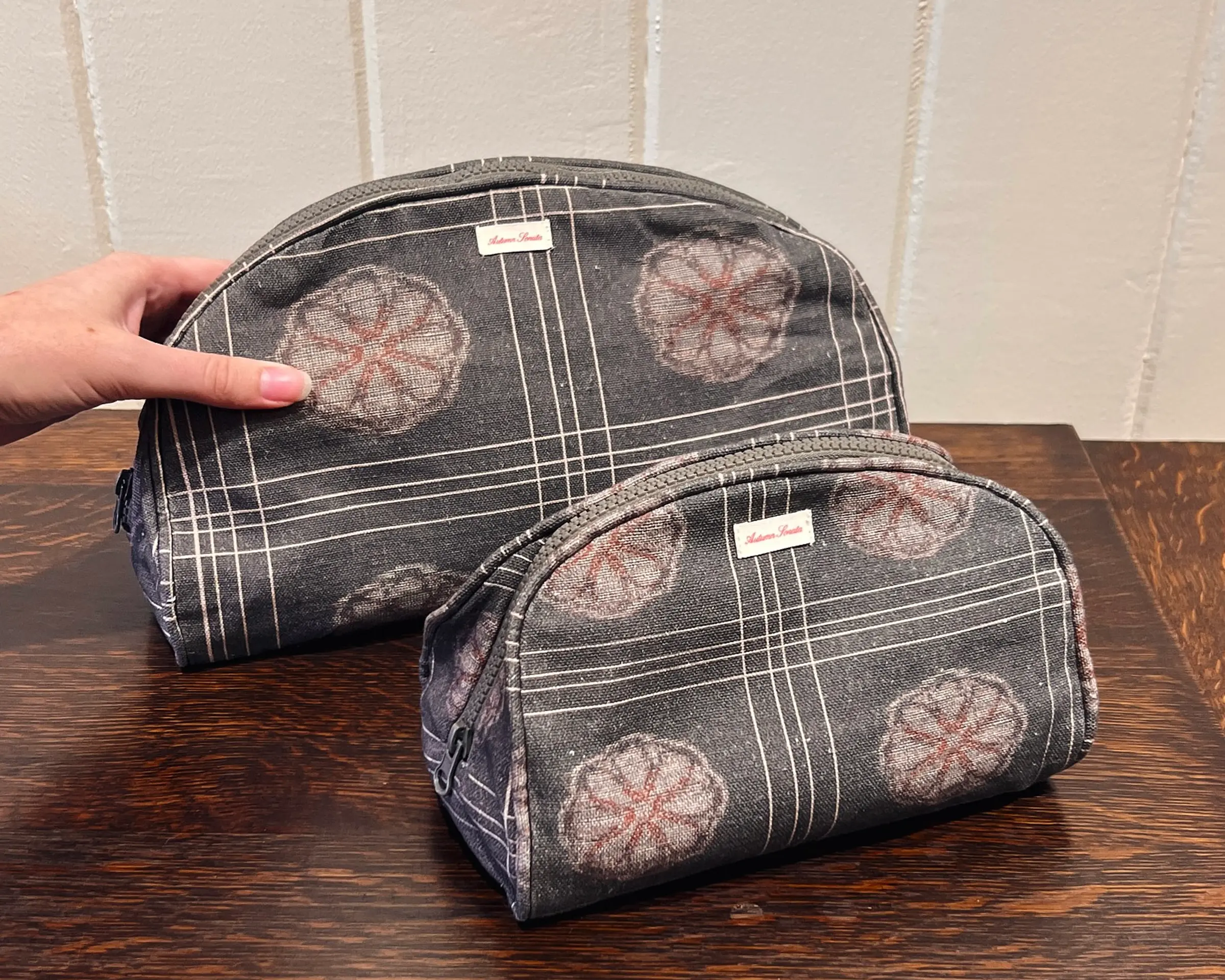 a hand picking up the Autumn Sonata Eva toiletry bag with the small infront of it