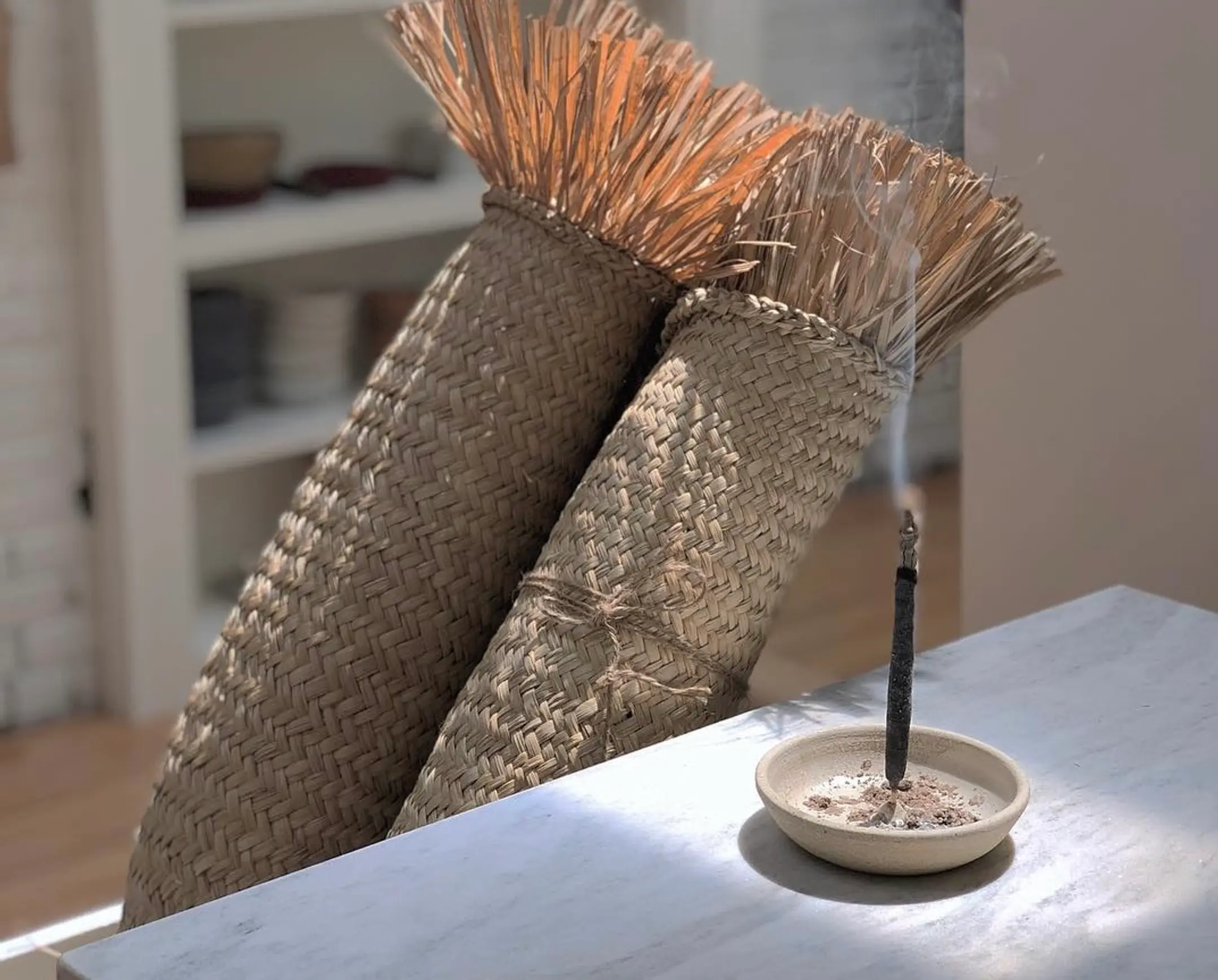 a palo Santo incense stick from Incausa burning on a tabletop with woven mats behind it