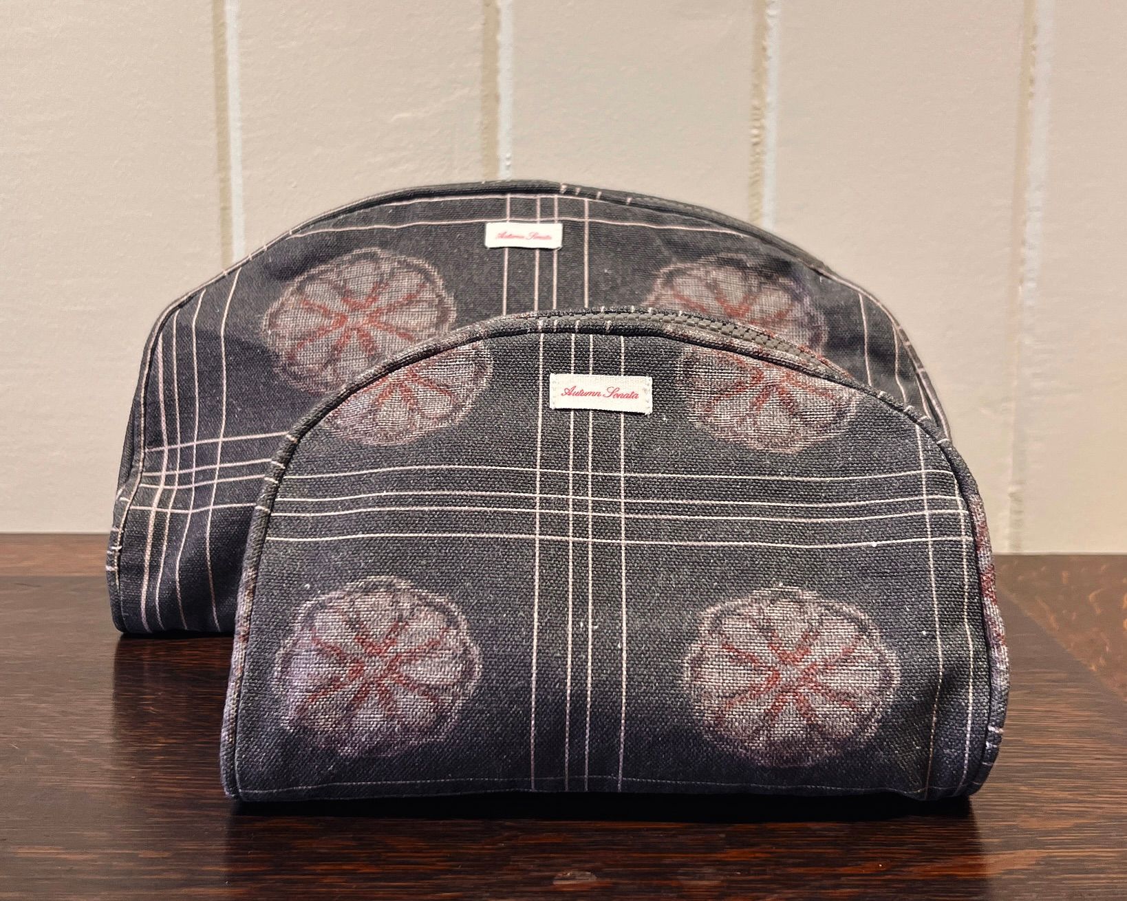 two of the Eva toiletry bags sat on a wooden table with a cream wall