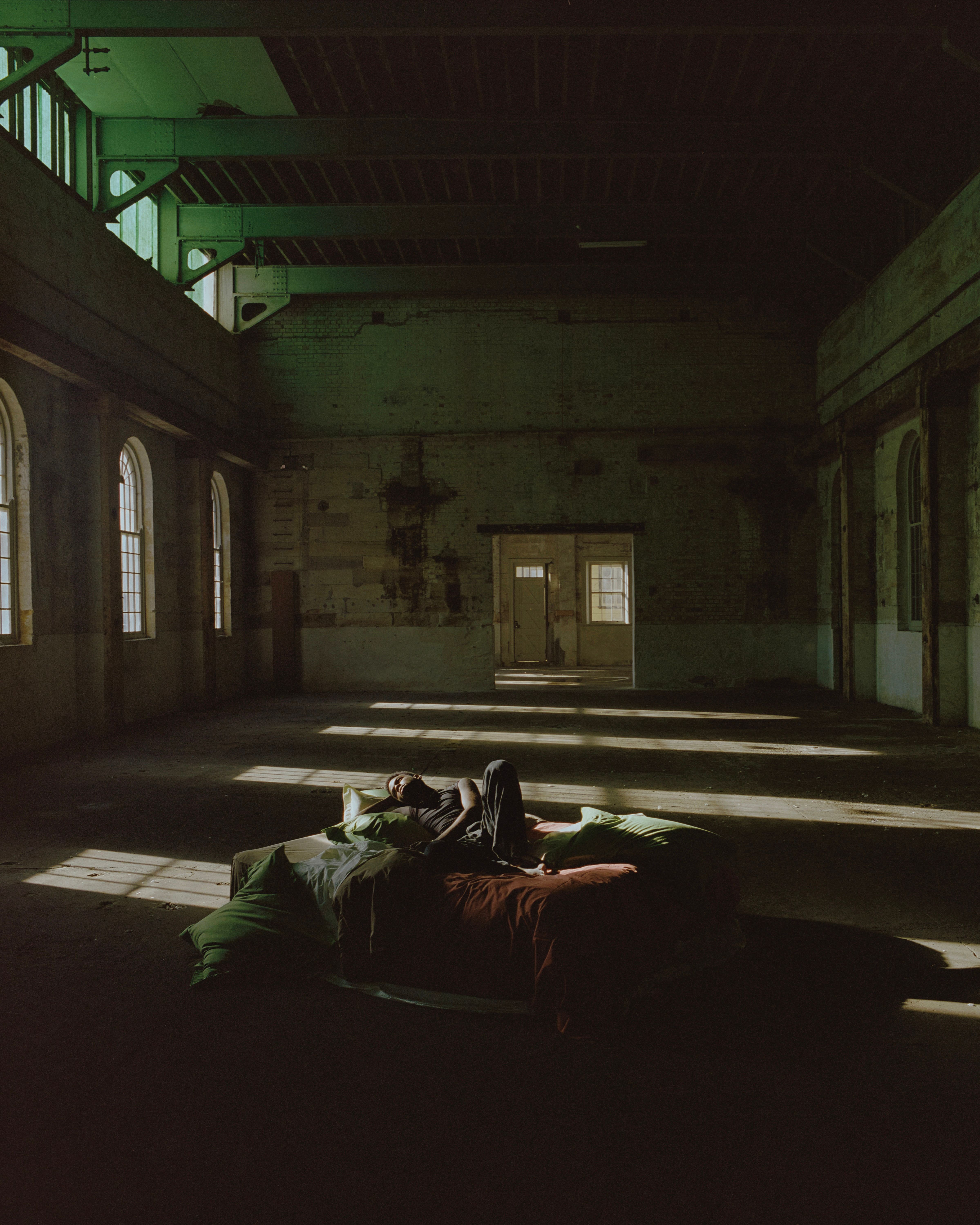 SUTRAM organic cotton bedding styled in a historic industrial building, featuring layered green and brown bed linen illuminated by natural light.