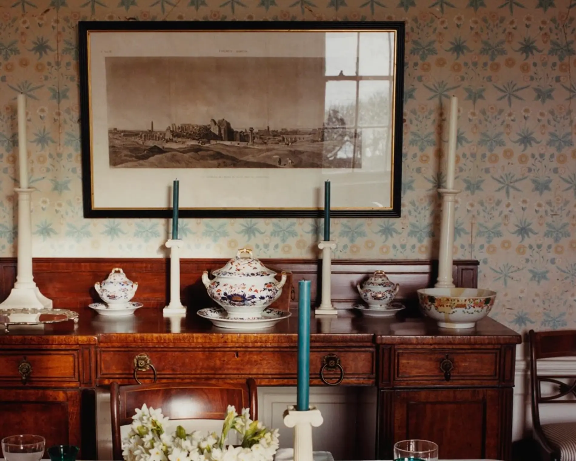 An image from Scenery magazine number 5, a wooden side board of in a living room filled with antiques, candle holders, ceramic and porcelain bowls