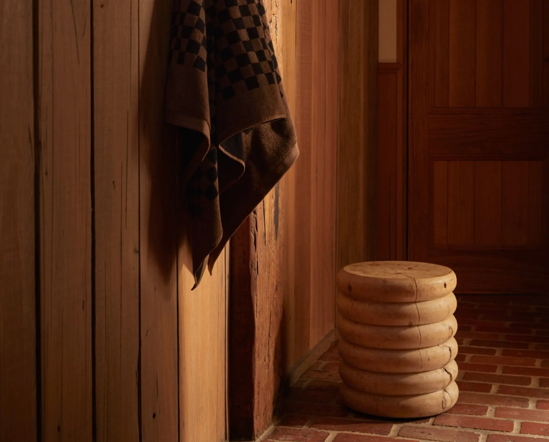 Brown and black checkered bath towel hung on the wall with a small wood stool next to it