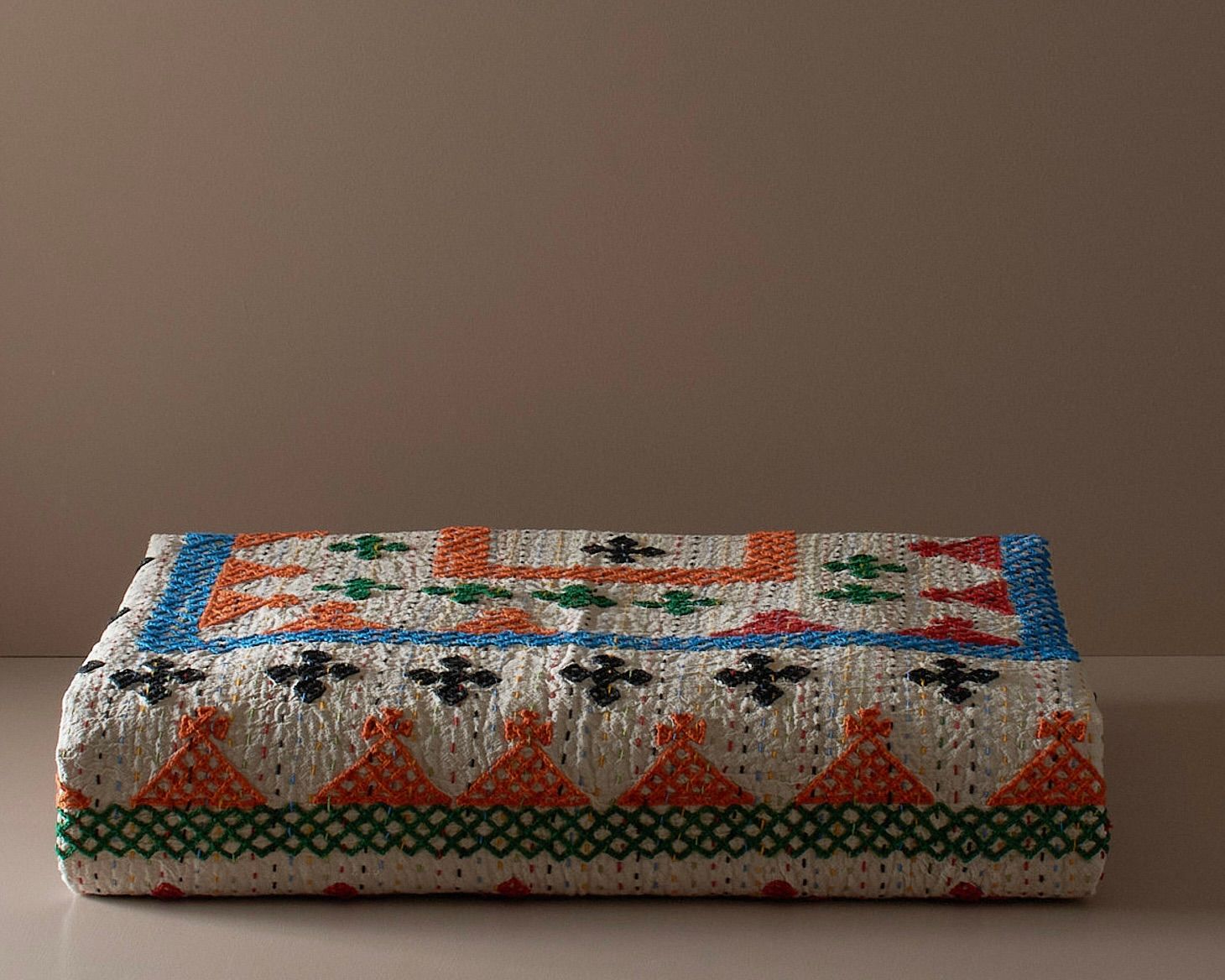 A Cross-stitch cotton Kantha bedcover on a neutral plinth