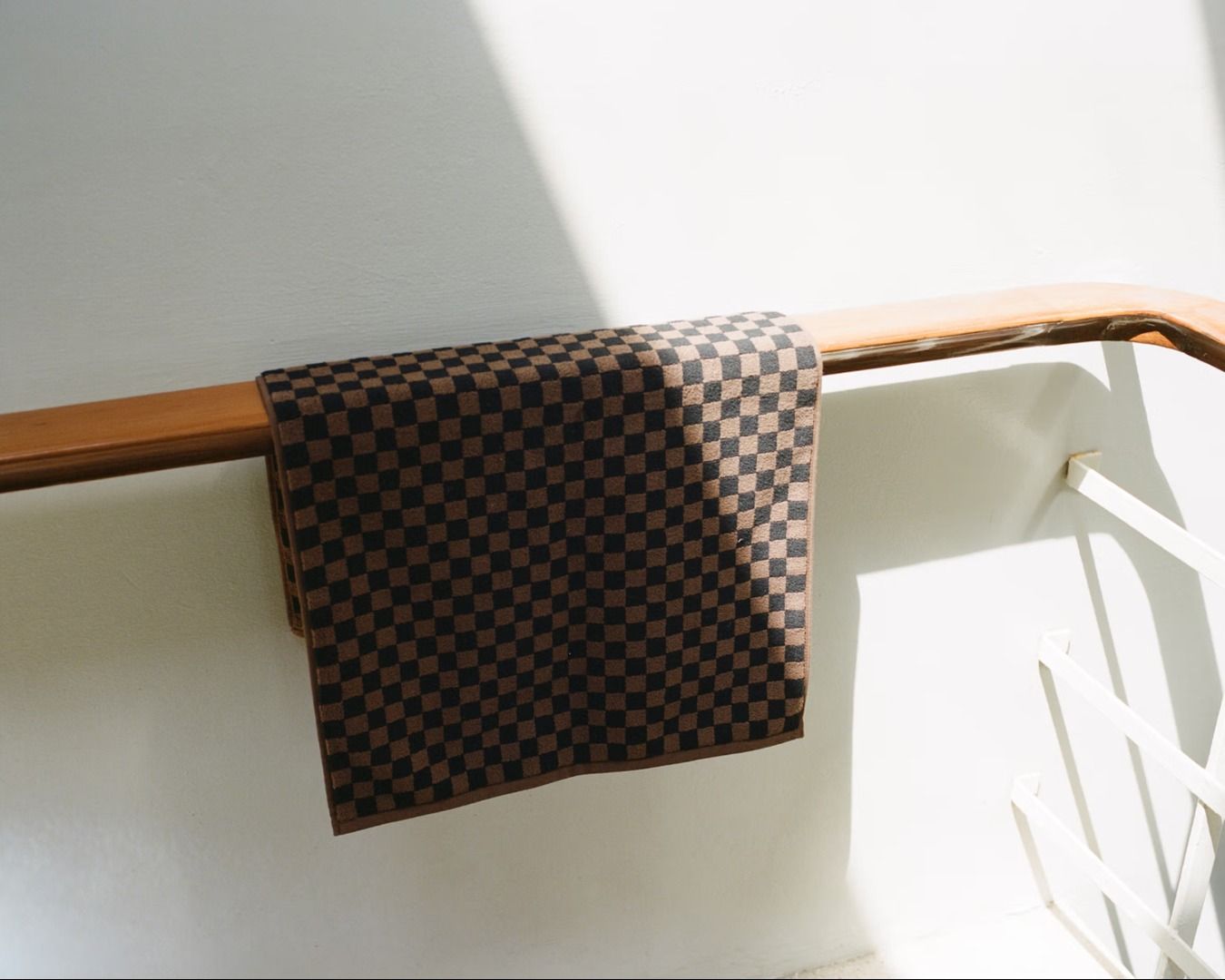 Black and brown checkered bath mat hung on a wooden railing in a staircase with white walls