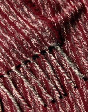 A close up detail shot of Burels Manta lumens merino wool blanket in a herringbone pattern with tones of grey cream and deep burgundy red