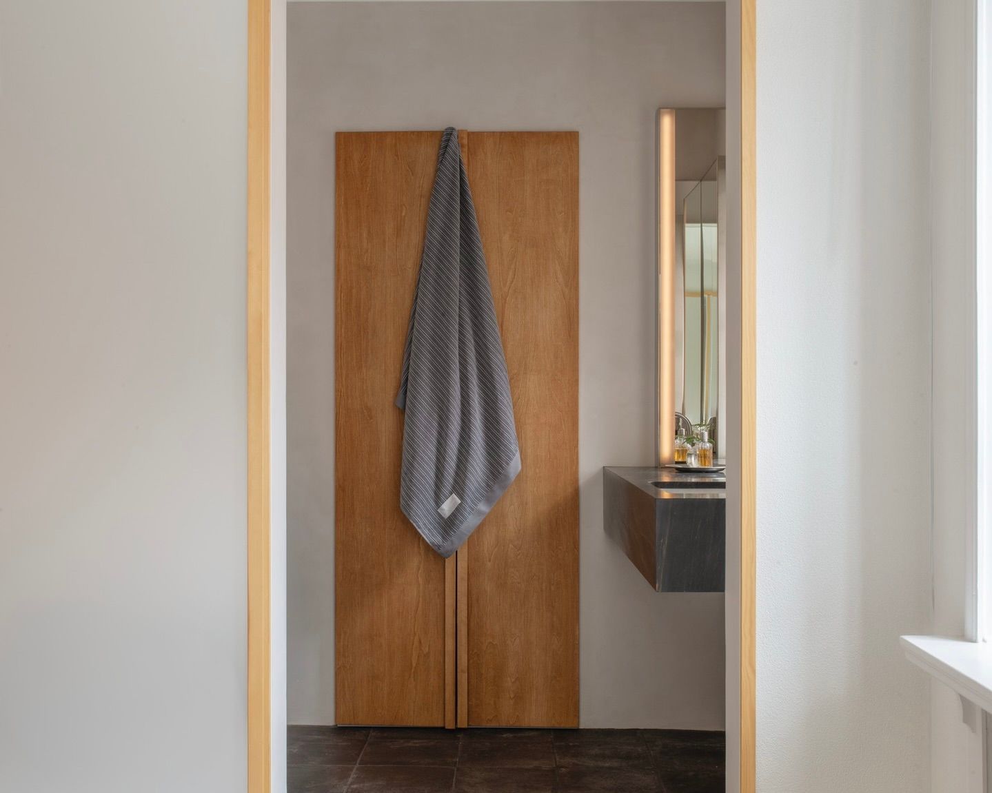 The Magniberg Wall Street dark grey striped towels hanging on a wooden cupboard in a minima listing style bathroom