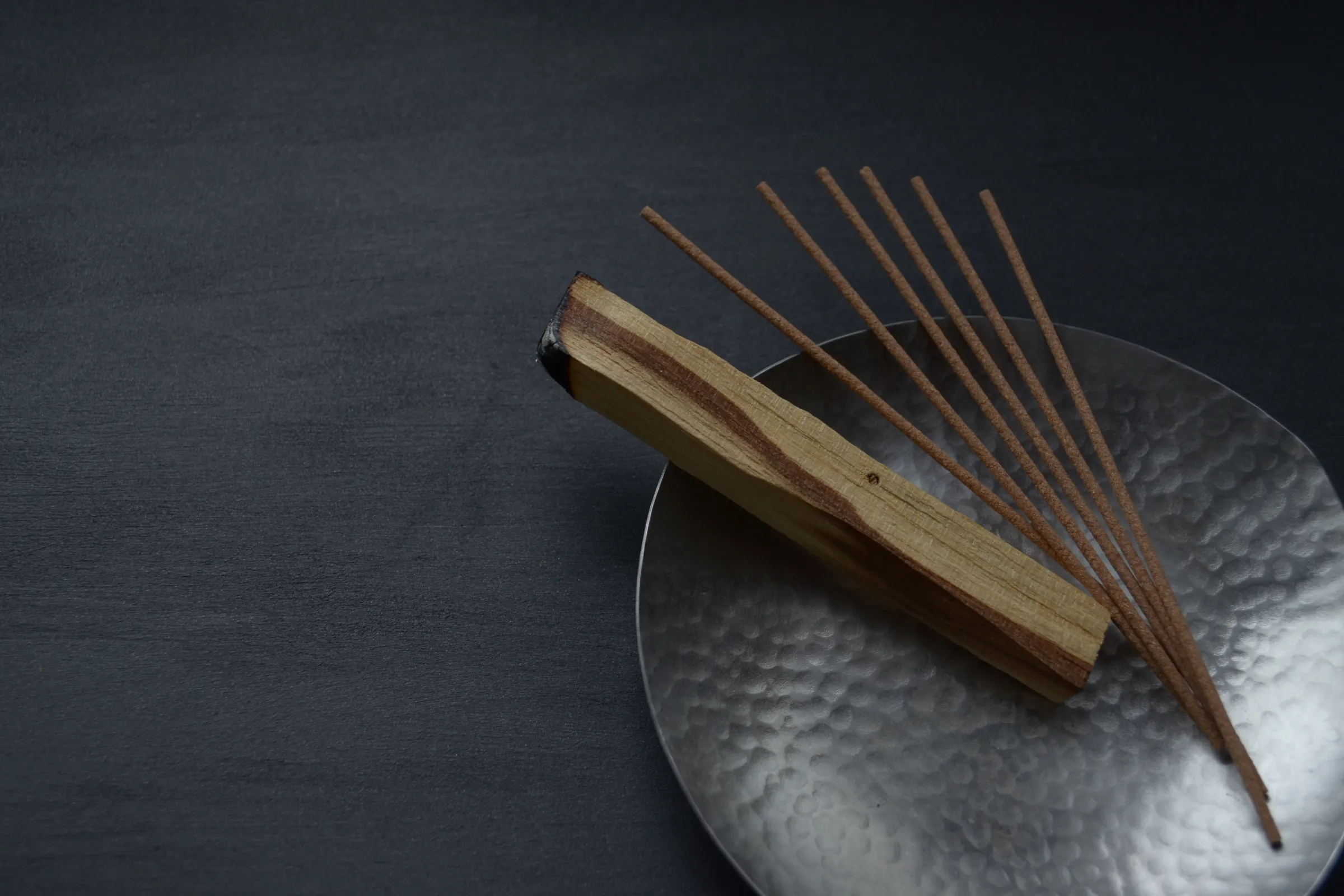 Incense sticks on a heated metal bowl next to a piece of agarwood