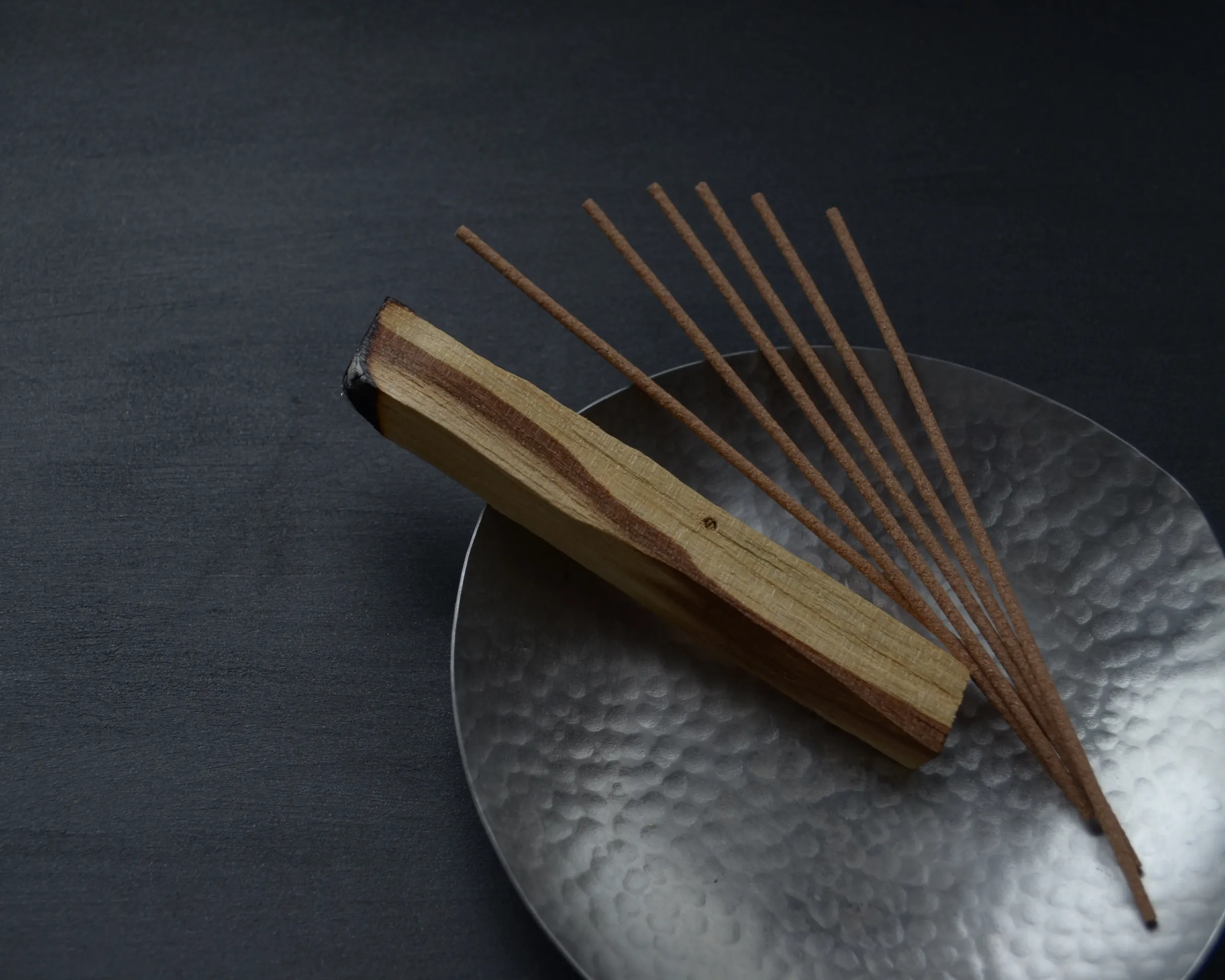Incense sticks and wood on a silver metal plate on a deep charcoal background