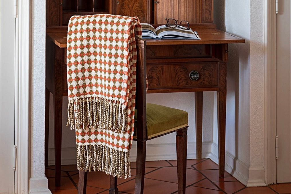 a Burel blanket hanging over a wooden chair with a desk set up infront of it