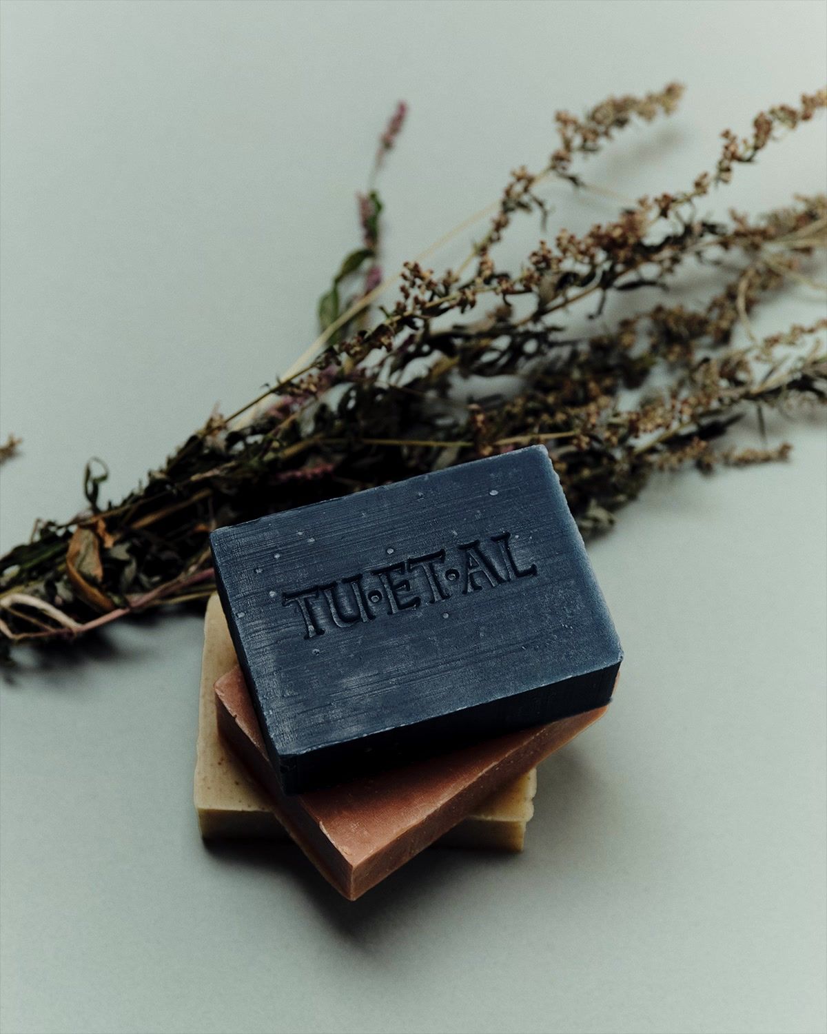 A Tuetal soap stack on a neutral background with a bundle of dried herbs