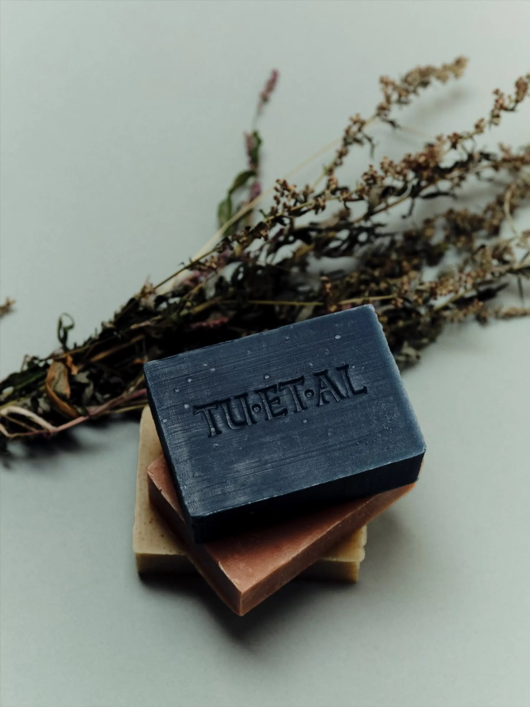 A Tuetal soap stack on a neutral background with a bundle of dried herbs