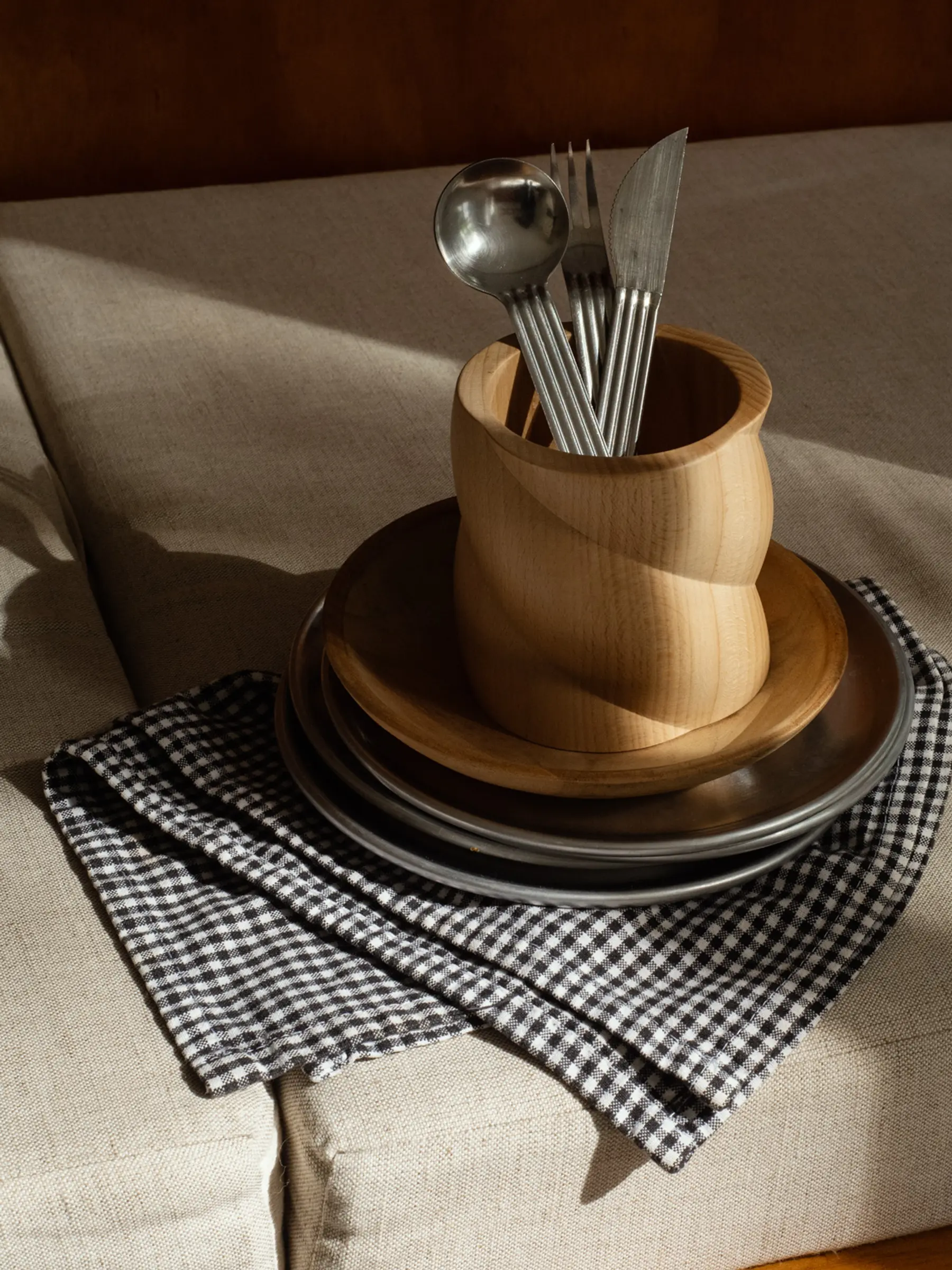 a small Torsade Collection hand turned cutlery holder with cutlery, sitting on a plate and napkin on a tabletop