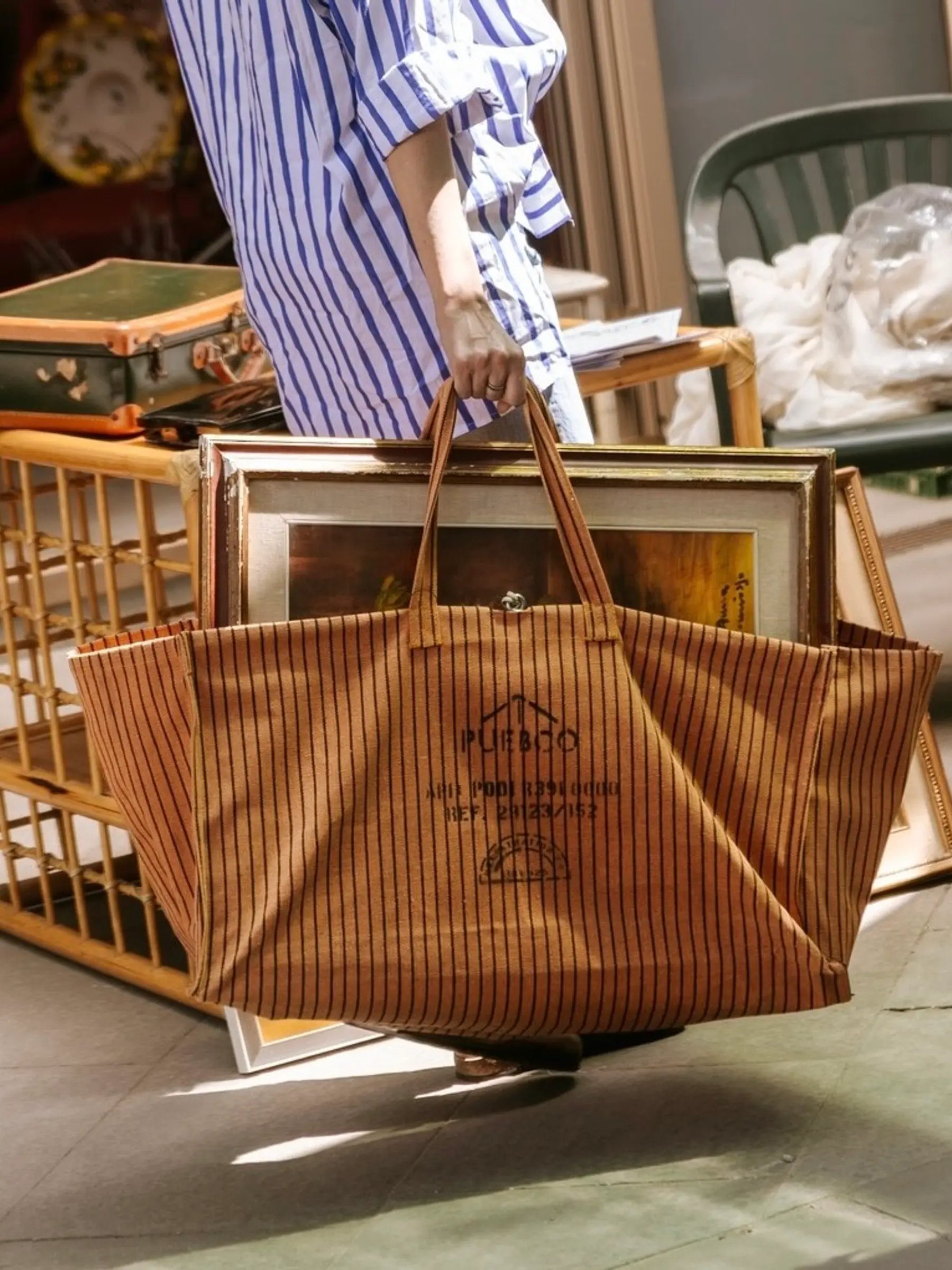 A woman carrying the Puebco Large waxed tote bag with a painting inside of it around a market