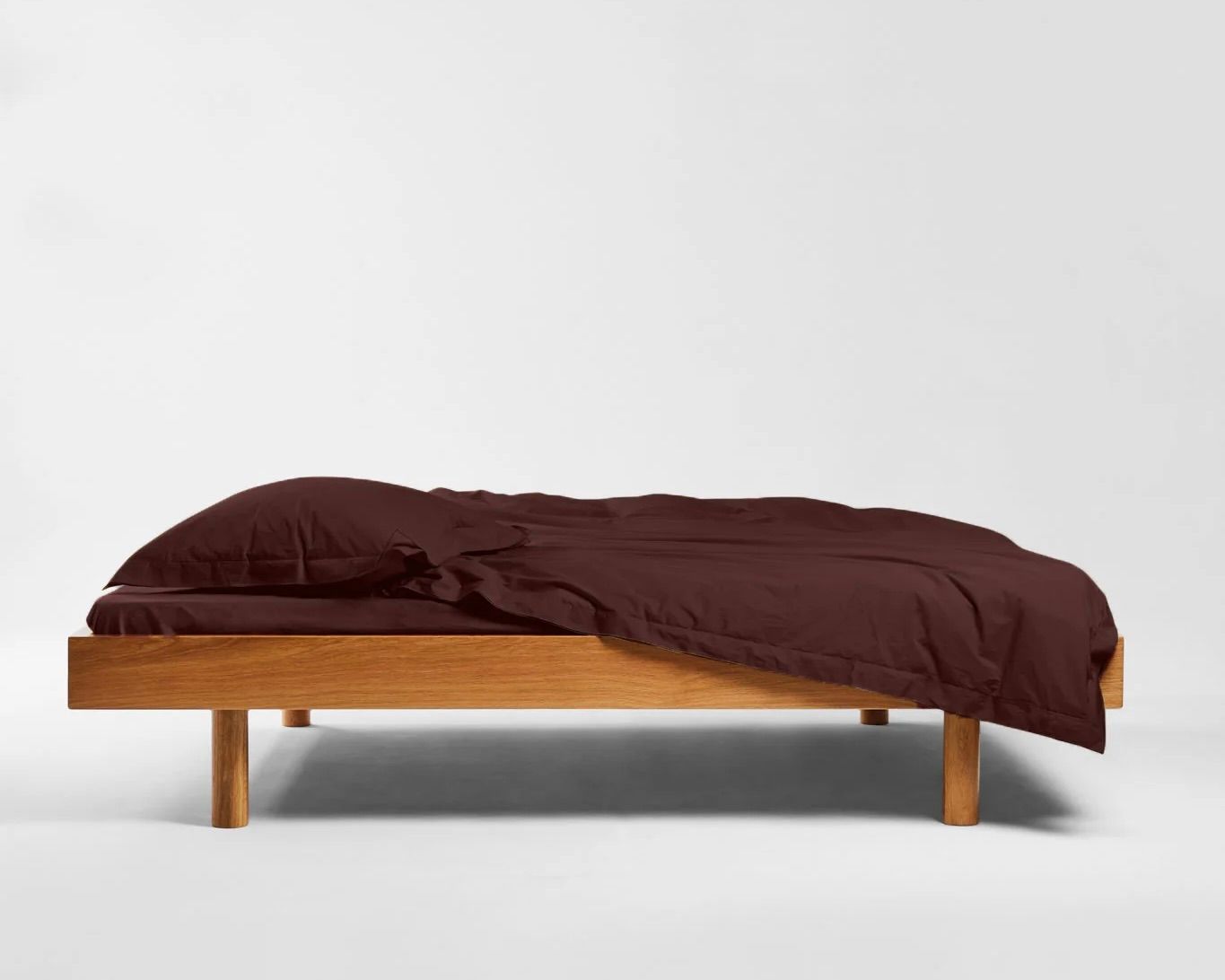 SUTRAM Eggplant Organic Cotton Percale Fitted Sheet woven in Portugal with a fully elasticated edge and generous mattress depth. Sutrams organic percale cotton bedding on a wooden bed frame with the sheets draped over the edges in the colour Eggplant, a rich deep aubergine, purple brown colourway
