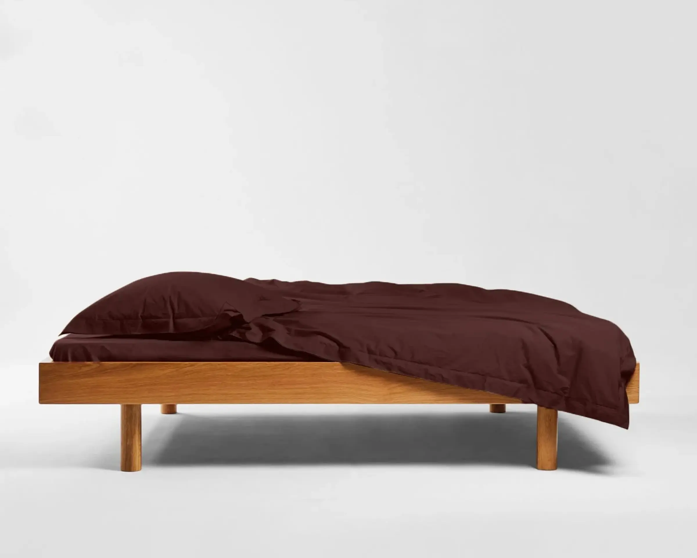 SUTRAM Eggplant Organic Cotton Percale Fitted Sheet woven in Portugal with a fully elasticated edge and generous mattress depth. Sutrams organic percale cotton bedding on a wooden bed frame with the sheets draped over the edges in the colour Eggplant, a rich deep aubergine, purple brown colourway