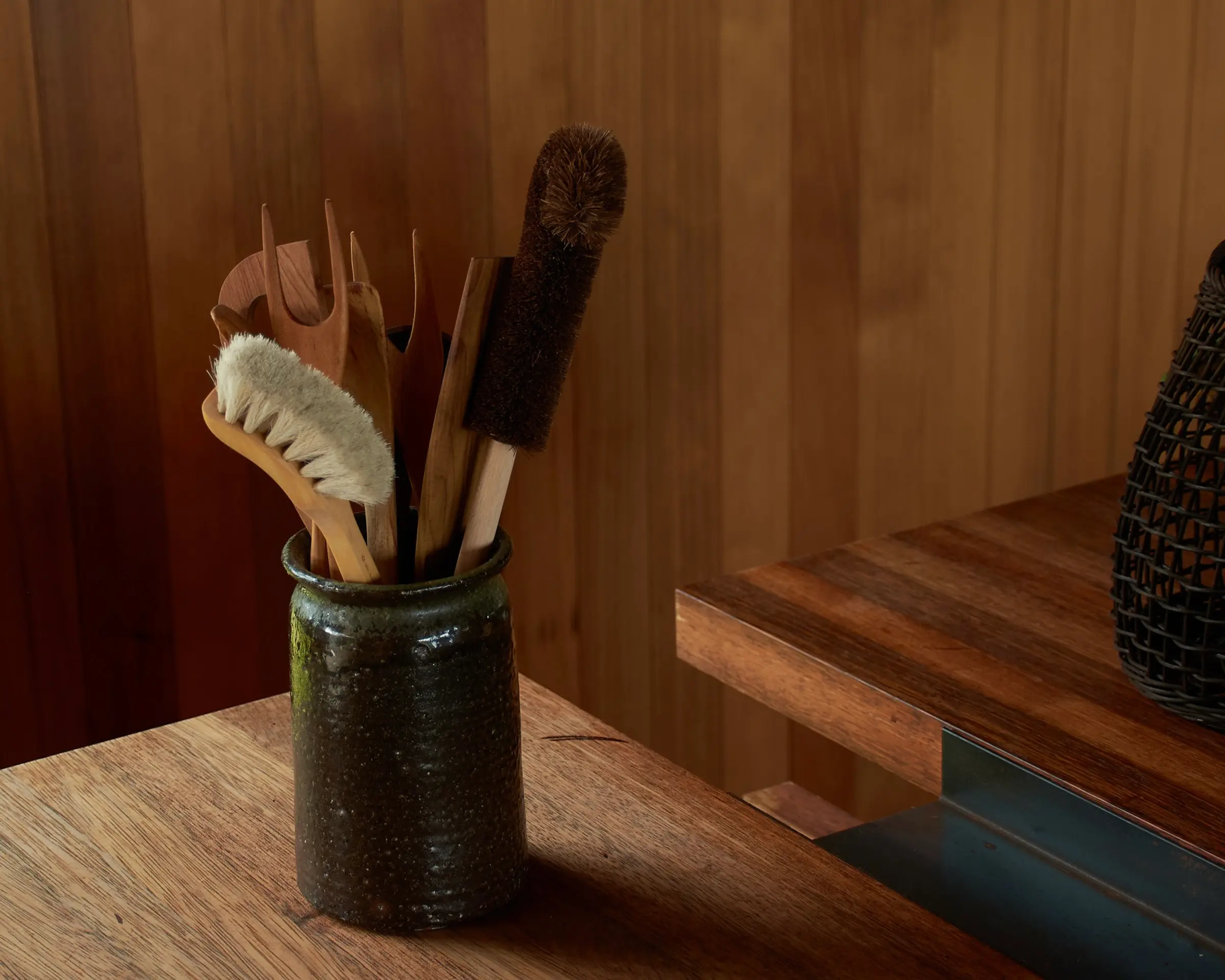 A ceramic vase with handmade wood utensils displayed on a wooden bench top