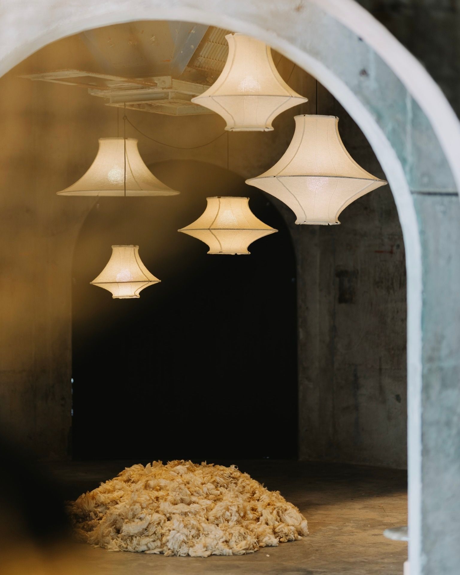 A collection of New Zealand strong wool made Wool Light pendants by Lof hanging in the Silo's in Auckland with a concrete archway with a pile of raw New Zealand Wool beneath them