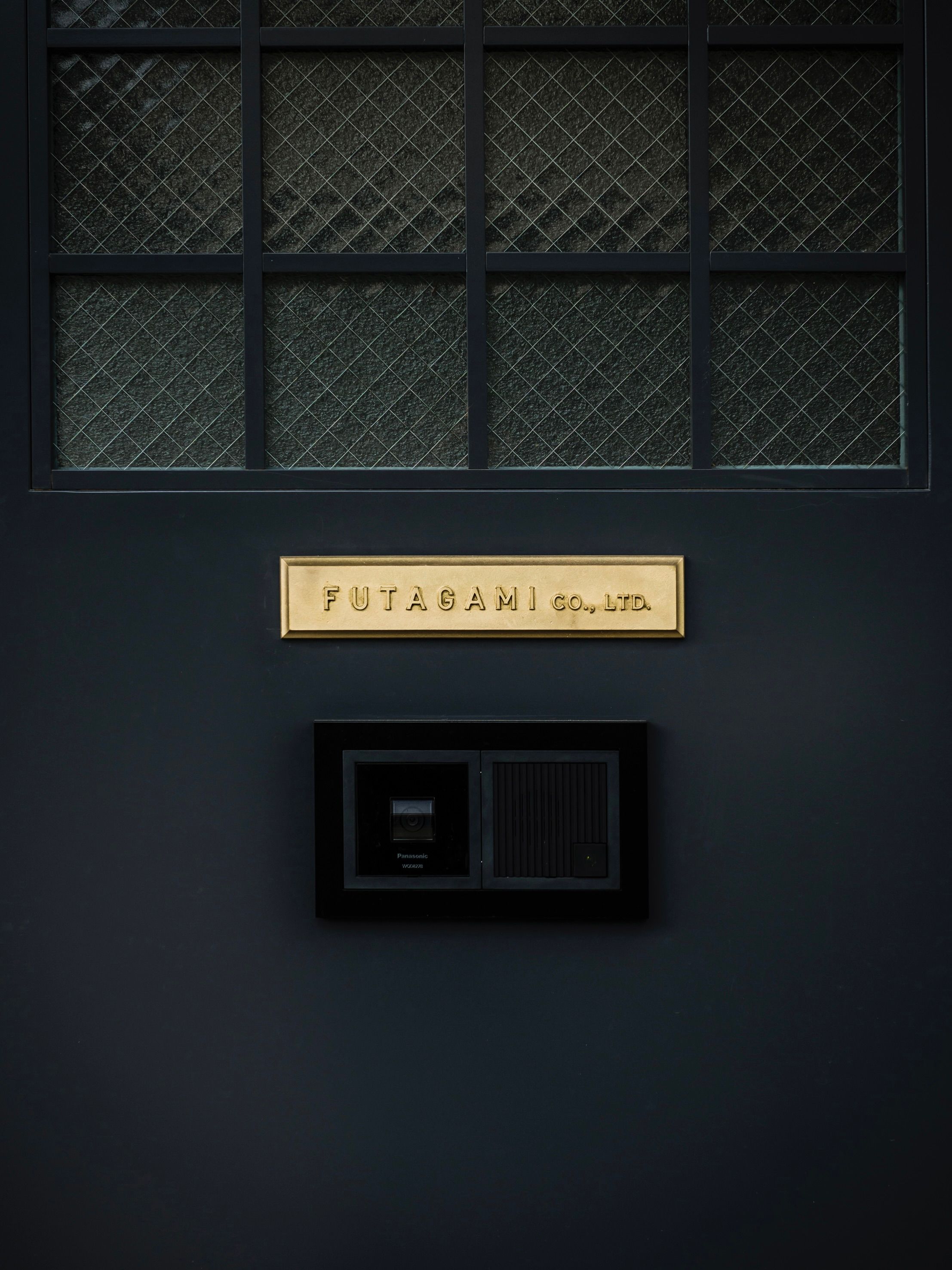 Futagami factory door painted black with a brass plaque sign.