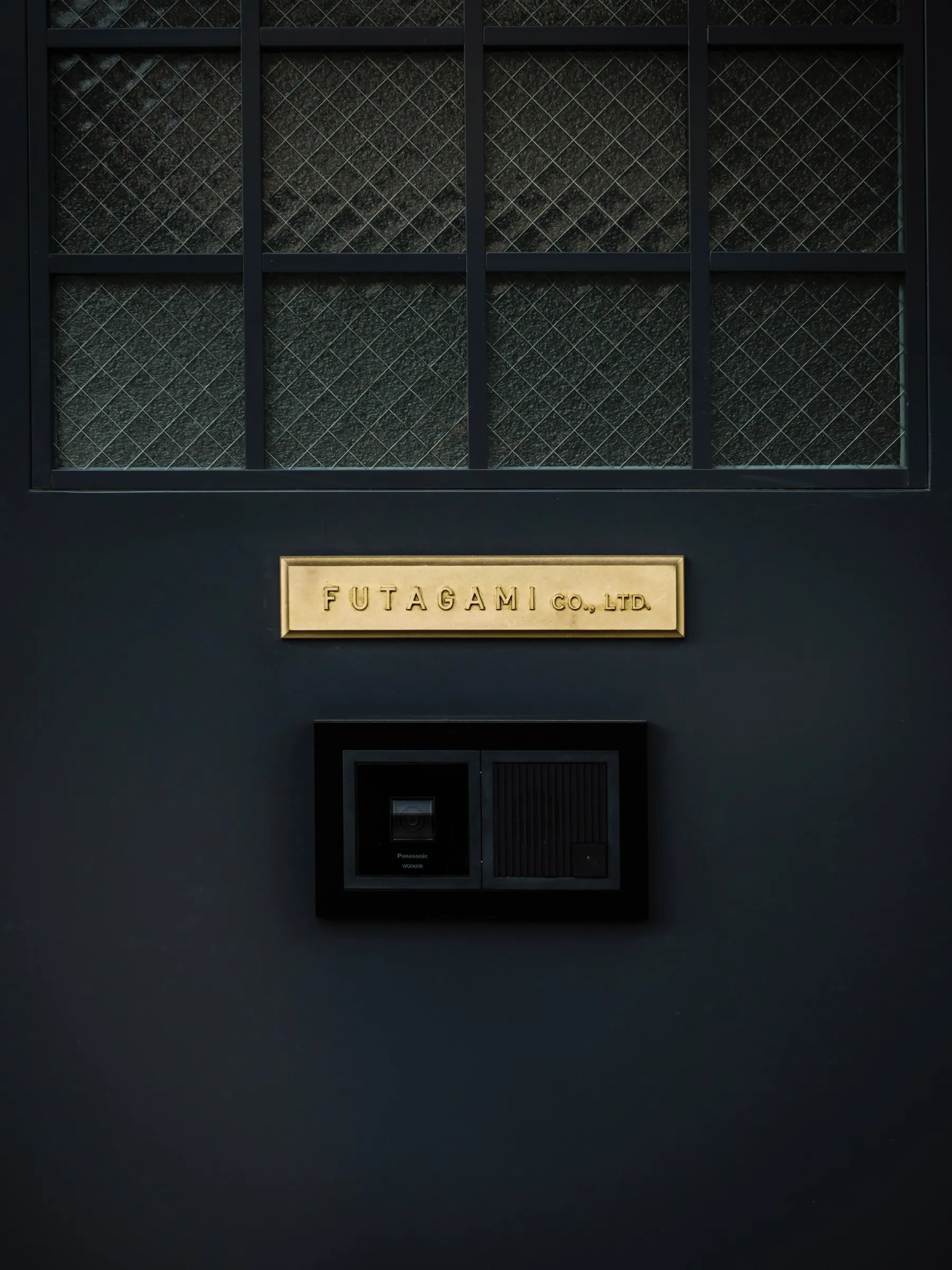 Futagami factory door painted black with a brass plaque sign.