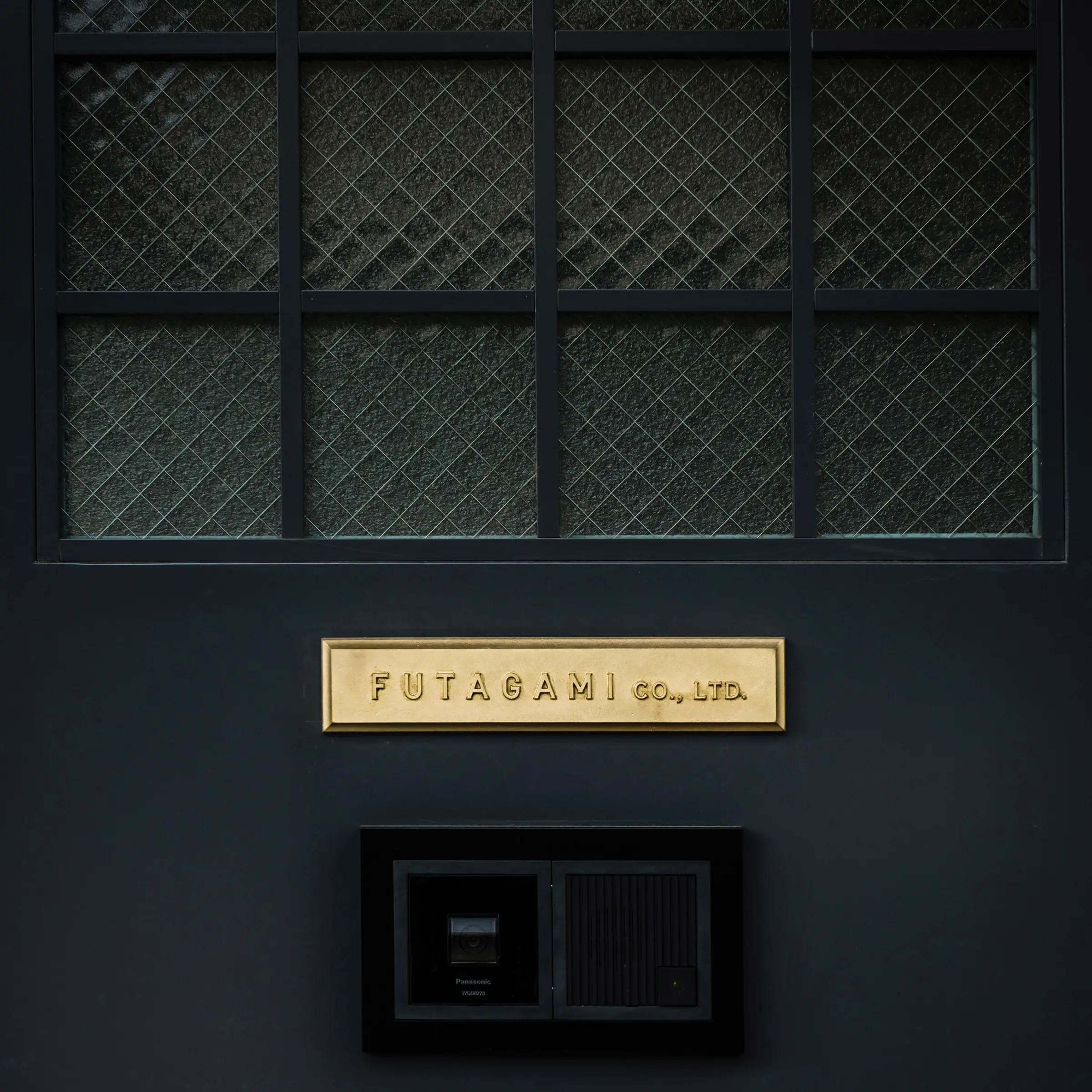 Futagami factory door painted black with a brass plaque sign.