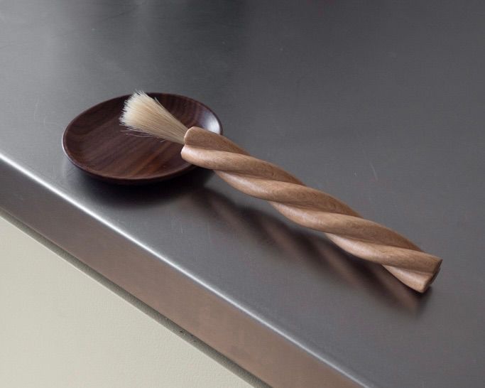 OROS Torsade kitchen brush in turned beechwood with blond horsehair bristles, shown with a wooden dish on a stainless steel surface.