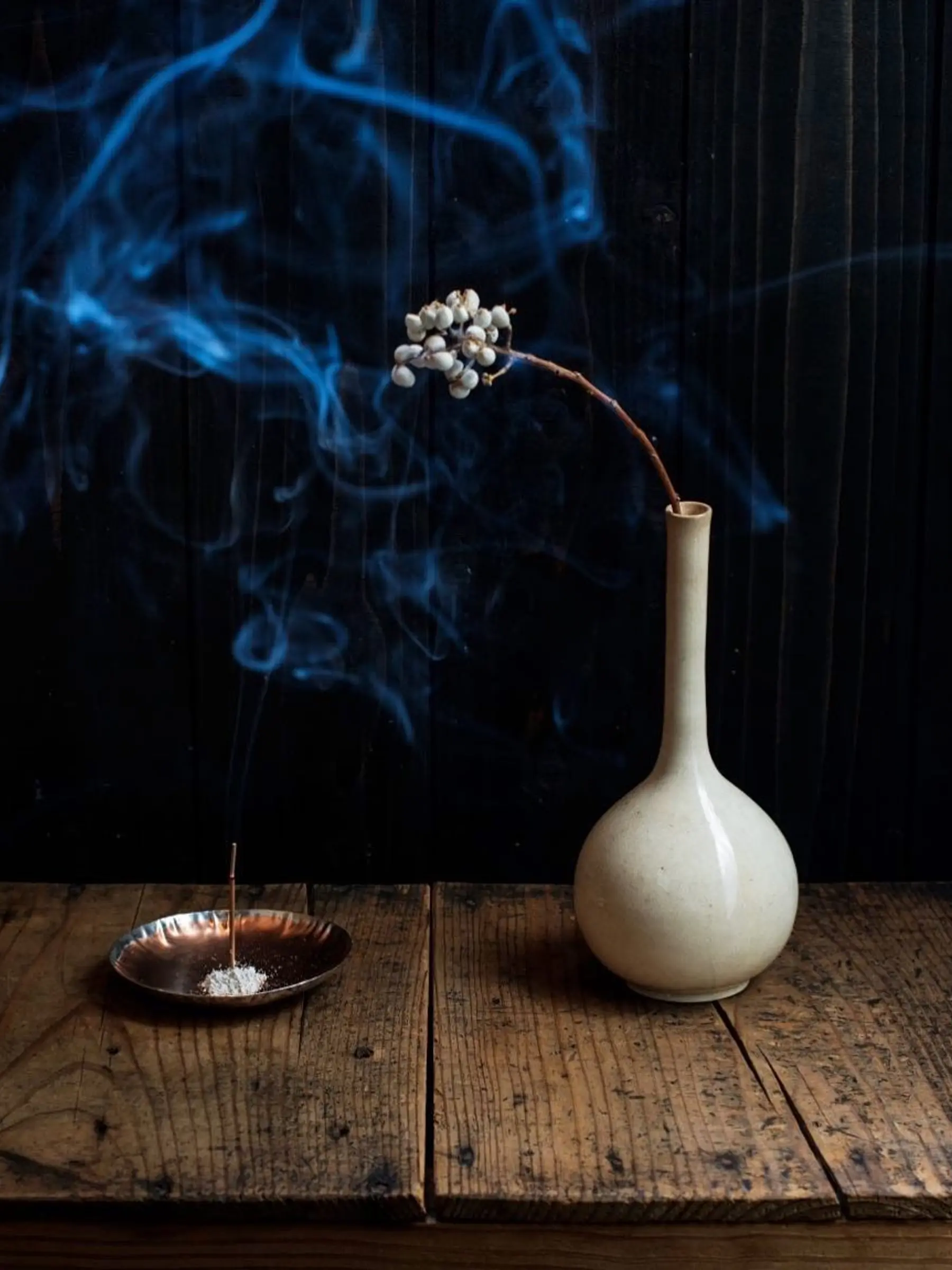 an image of incense burning on a wooden table with a small white vase next to it