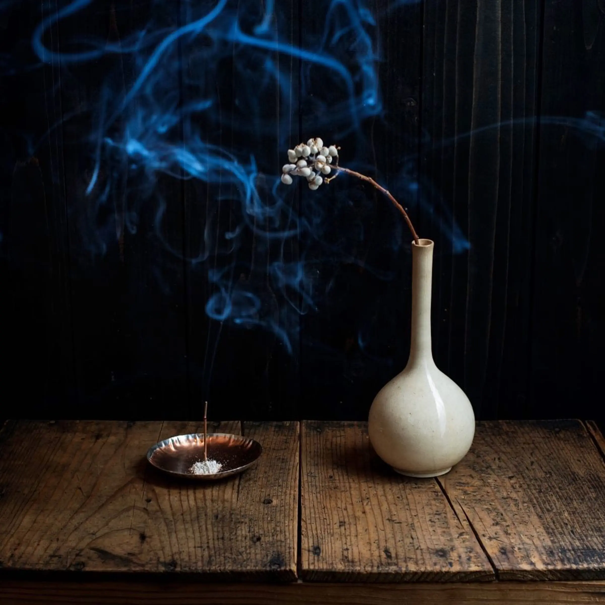 an image of incense burning on a wooden table with a small white vase next to it