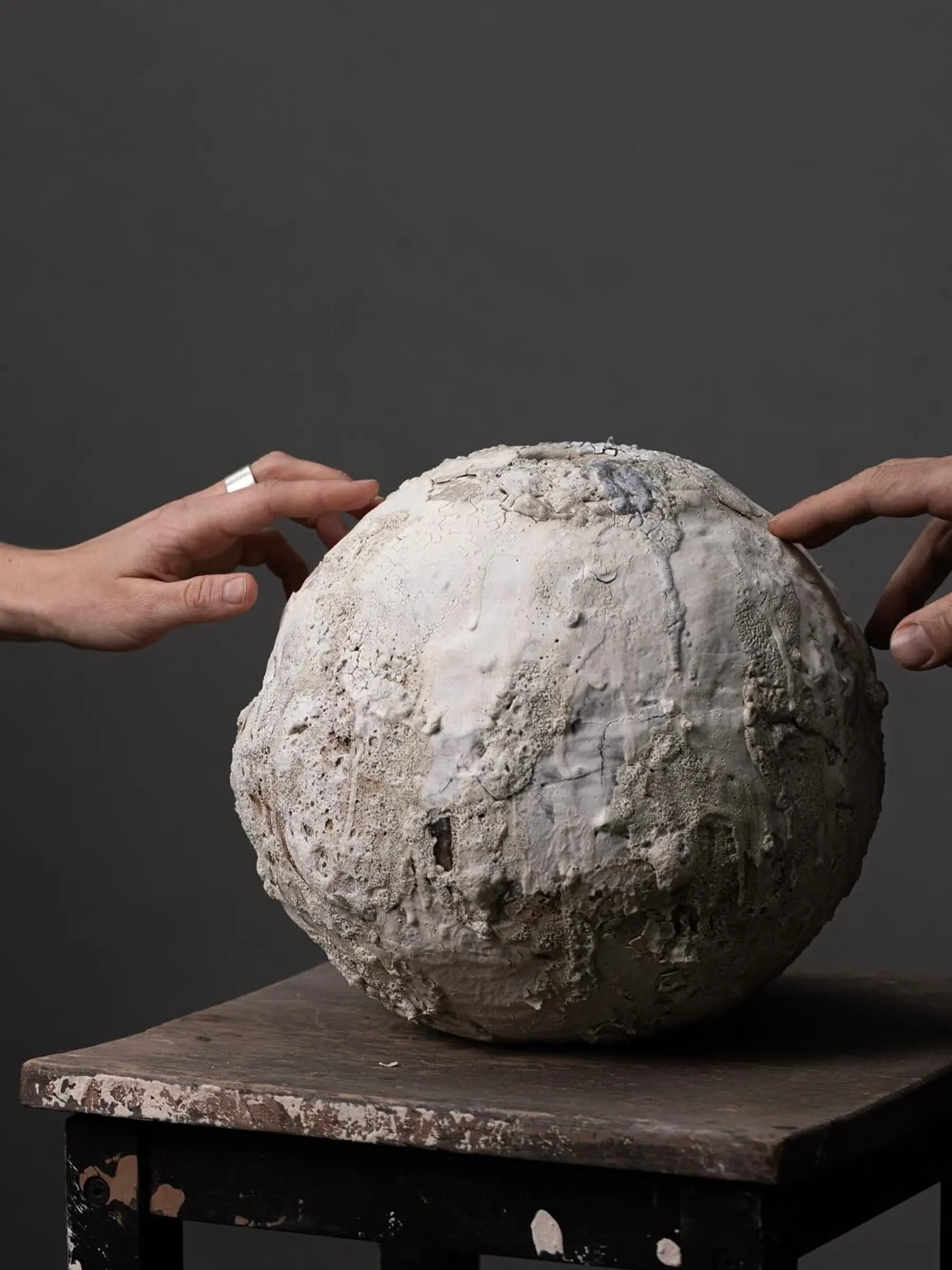 Loram Ceramics vase on a wooden stool with two hands touching the edges.