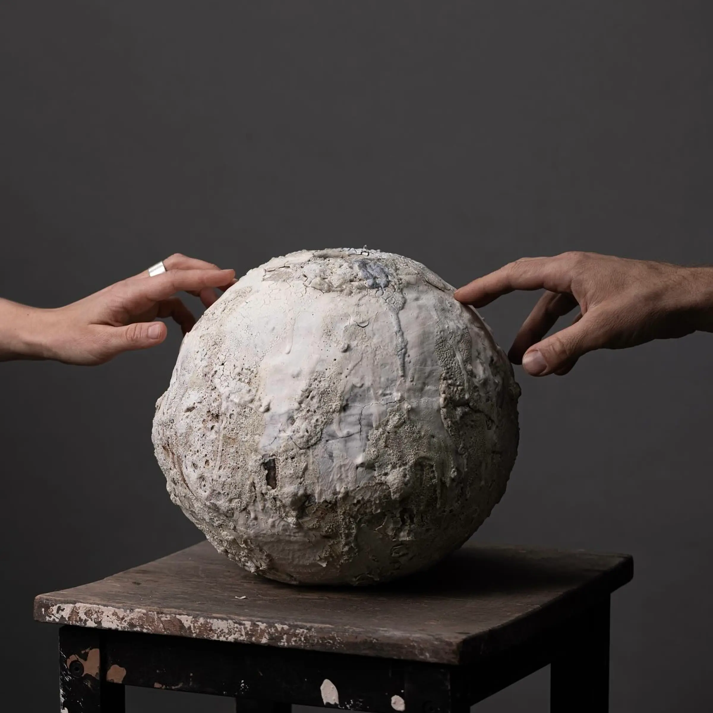 Loram Ceramics vase on a wooden stool with two hands touching the edges.