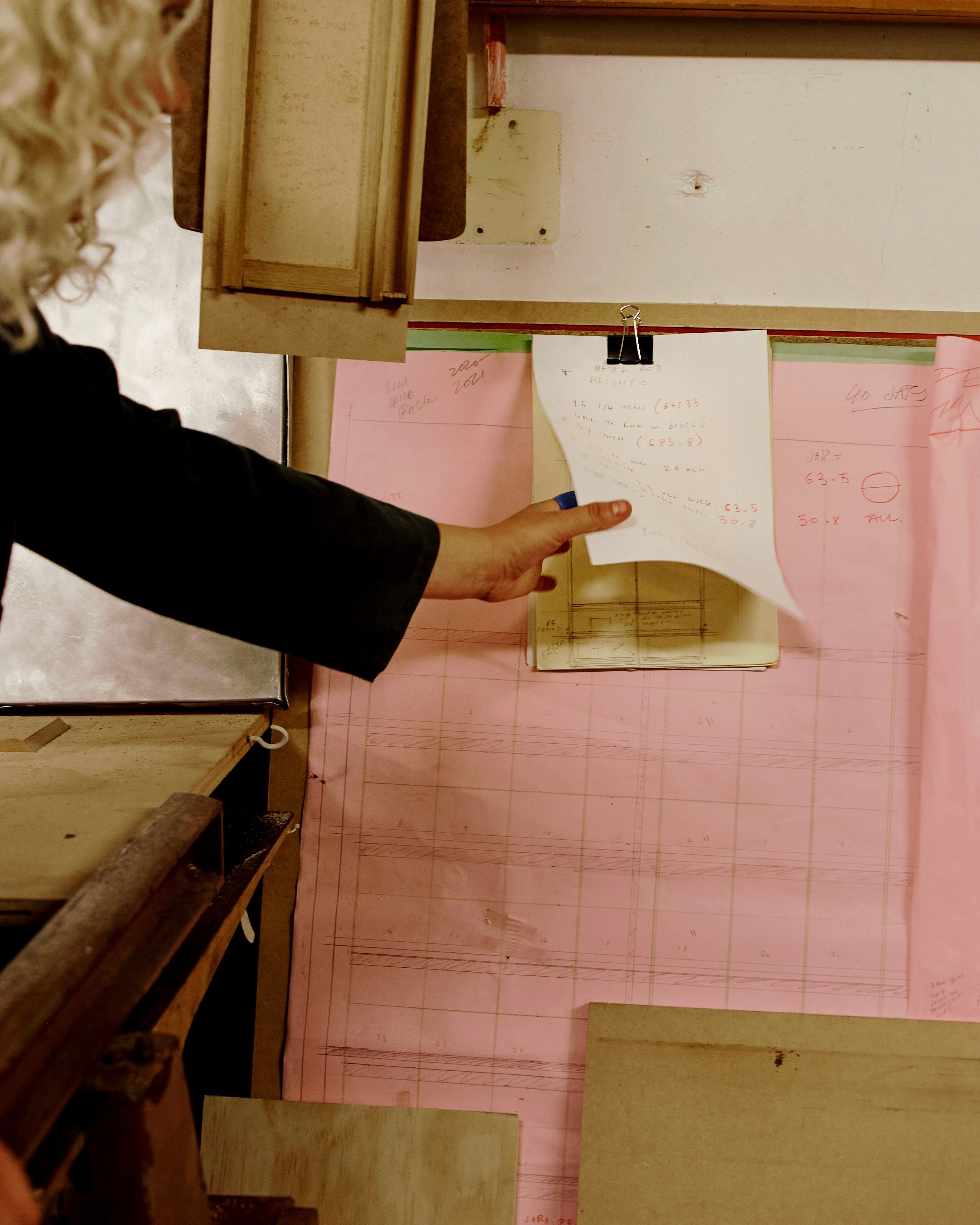 Josephines wood workshop with pink paper and a hand reaching for a sheet not he wall