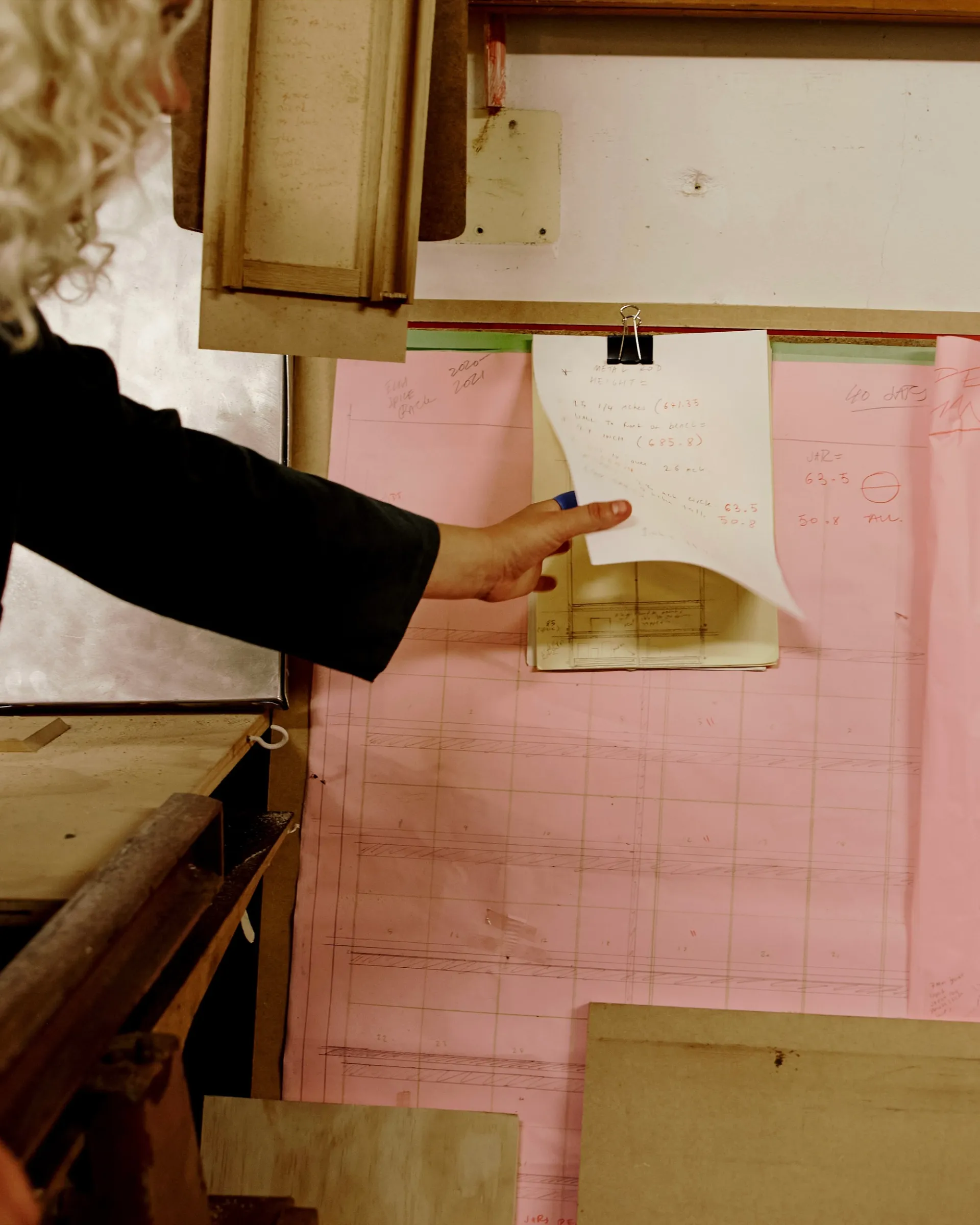 Josephines wood workshop with pink paper and a hand reaching for a sheet not he wall