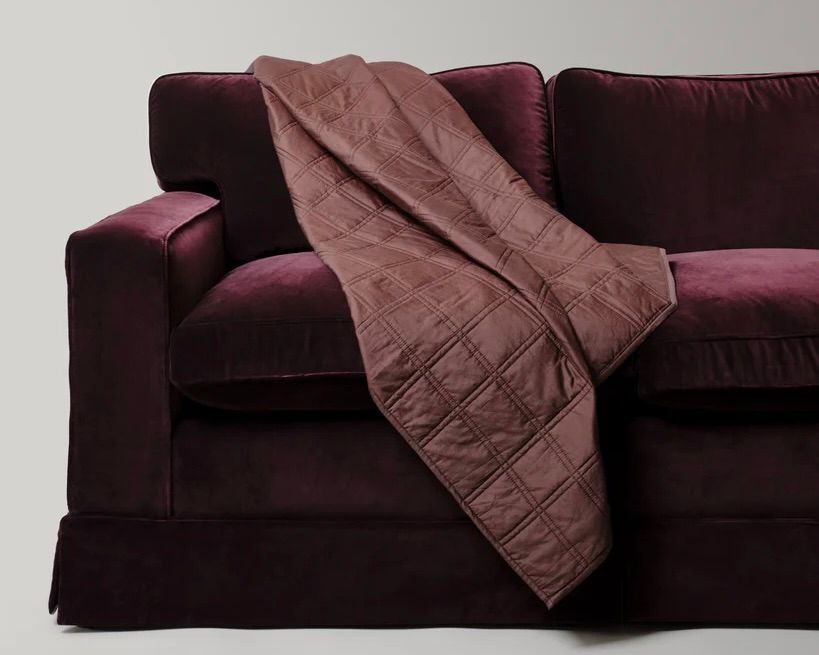 The Dhara Grid Throw by Studio Ford, woven from a silk-cotton blend and hand-dyed to a rich chocolate brown, subtle lustre that shifts beautifully with the light draped on a deep purple velvet sofa. 