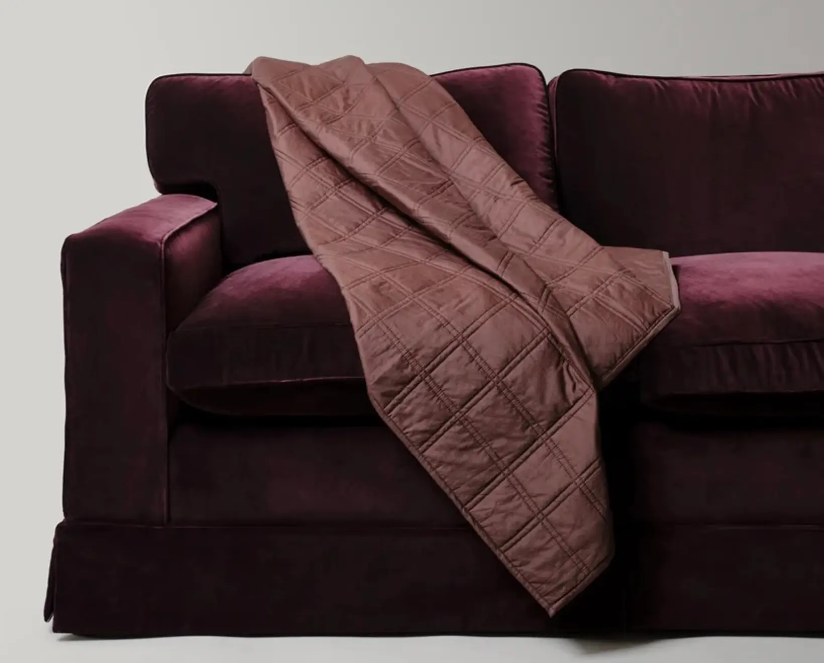 The Dhara Grid Throw by Studio Ford, woven from a silk-cotton blend and hand-dyed to a rich chocolate brown, subtle lustre that shifts beautifully with the light draped on a deep purple velvet sofa.