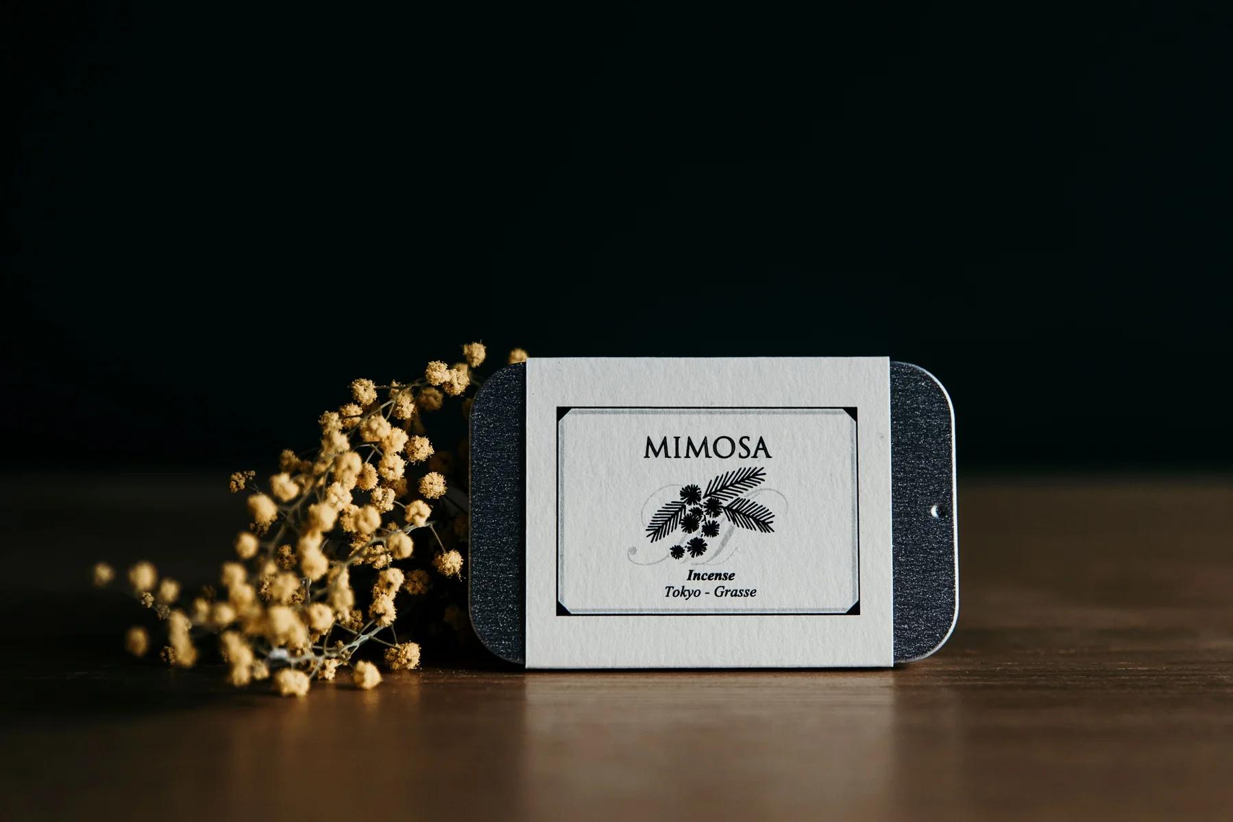 Mimosa tin of incense with small yellow bud flowers on a wooden surface 