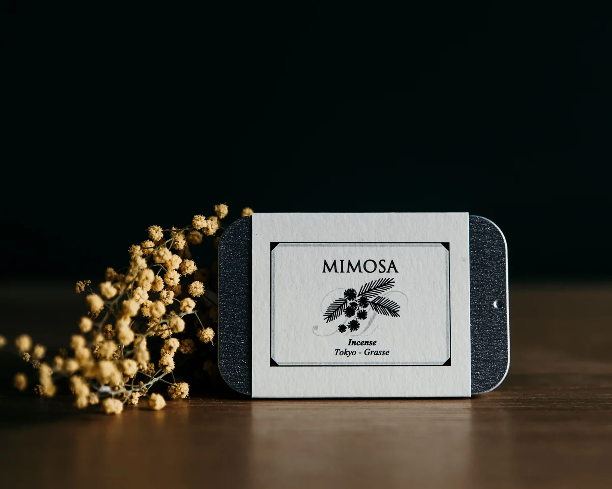 Mimosa tin of incense with small yellow bud flowers on a wooden surface