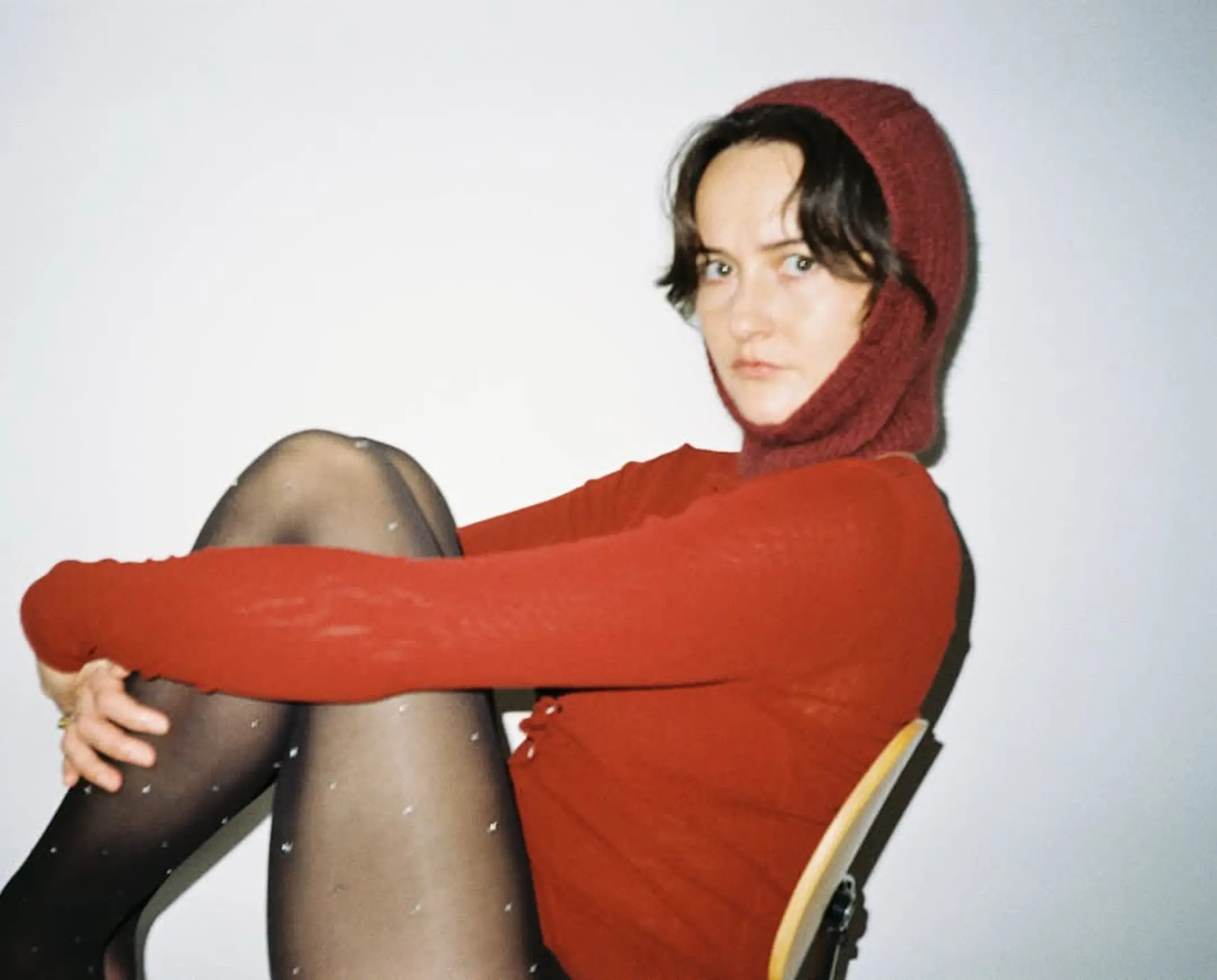 A woman wearing a Bonnie Wroe, possum merino yarn balaclava sitting on a chair