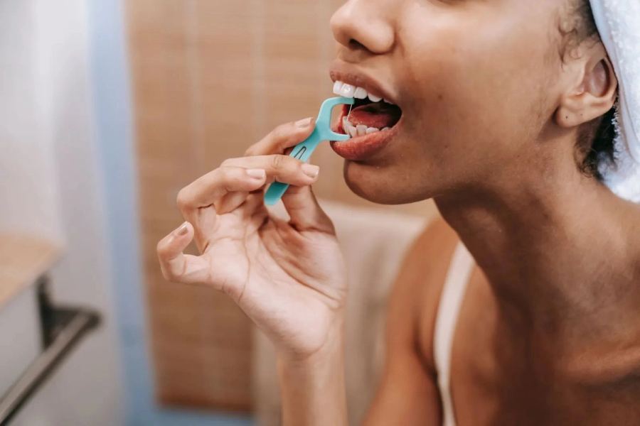 Someone using a floss pick in front of a bathroom mirror.