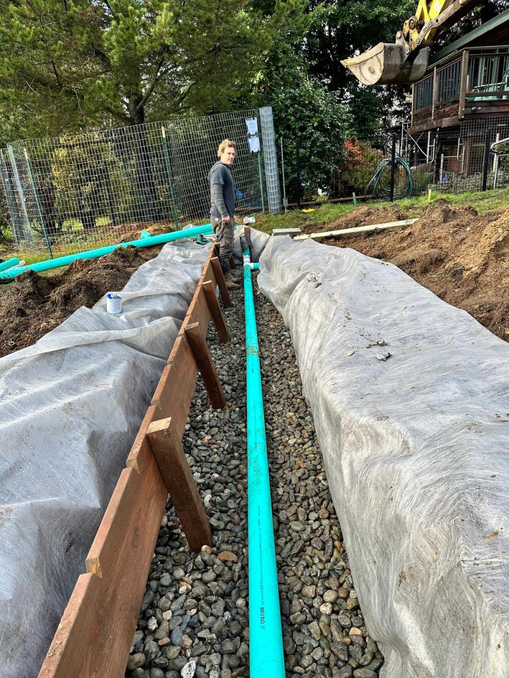 French drain with rigid PVC pipe on washed drain rock, wrapped in filter fabric