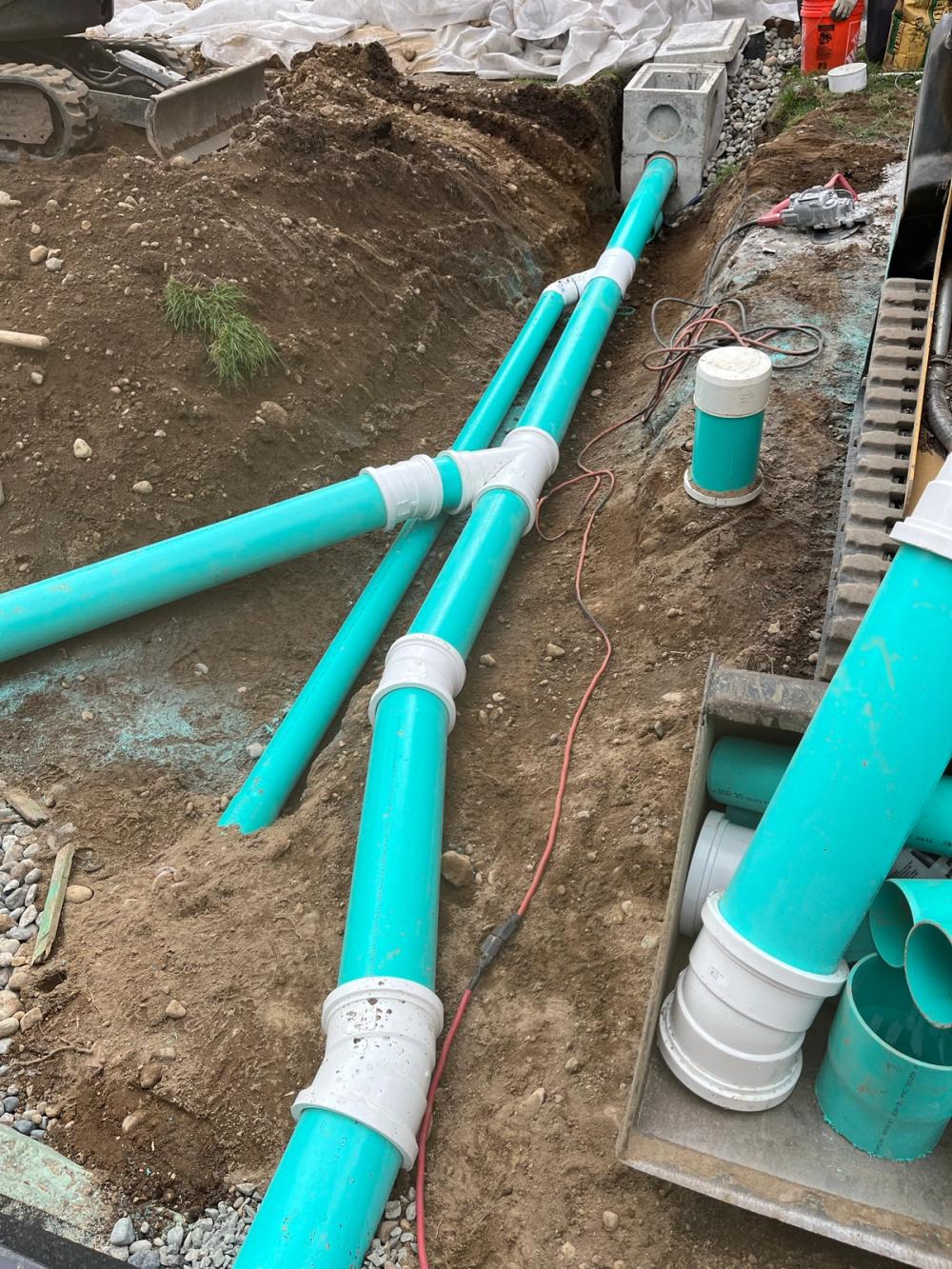 Rigid PVC drain lines joined with wye fittings, running to a catch basin with a cleanout