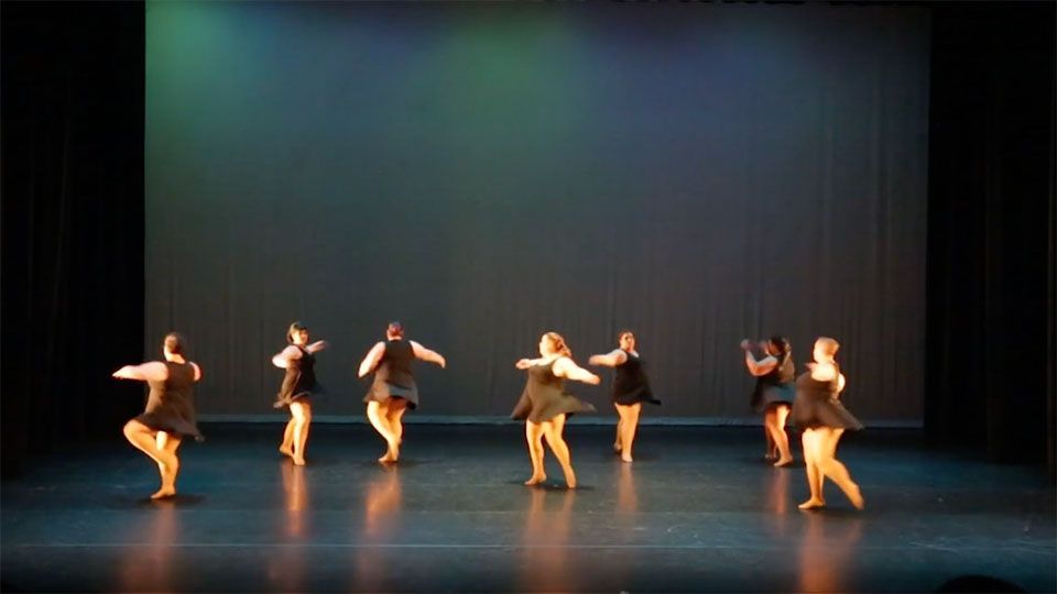 seven ladies in black dresses dancing on a large stage with black curtains