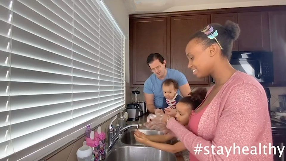 A young woman washes hands with her young children as Dad looks on