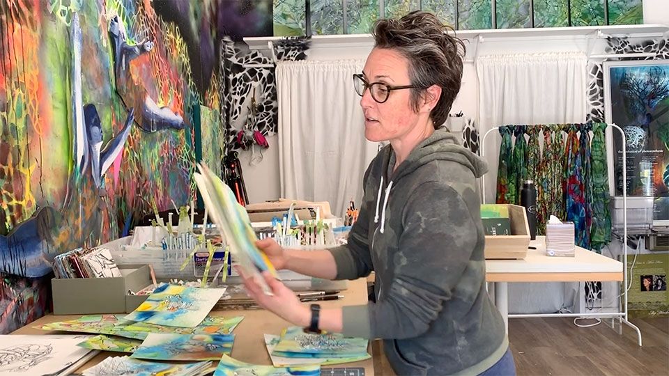 artist in studio and walls covered in paint is sorting her hand-held paintings