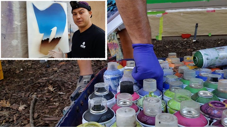 Young man demonstrating wall art using hundreds of different paint cans