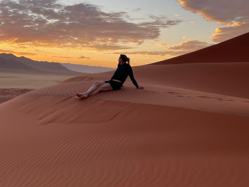 Peggy contemplando la puesta de sol desde una duna de arena en el desierto de Namib, cerca de Sossusvlei, Namibia.