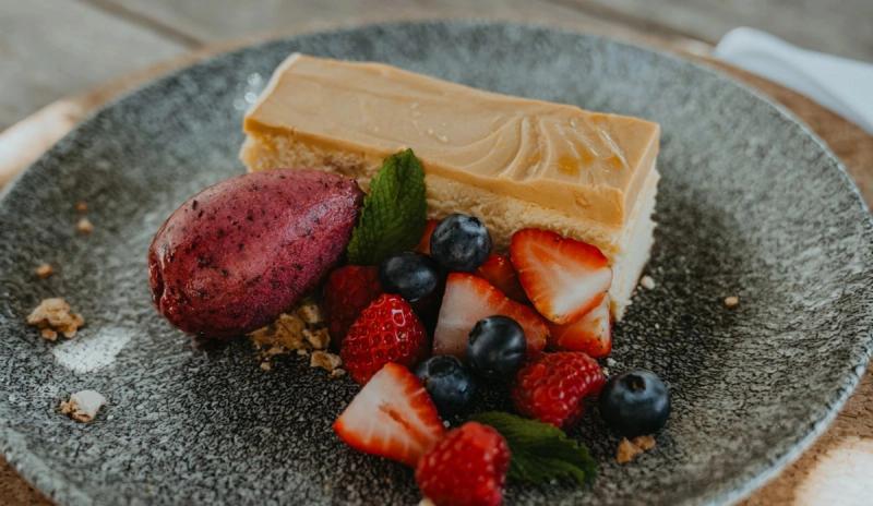 Slice of caramel cheesecake served with berry sorbet, strawberries, blueberries and mint on a plate