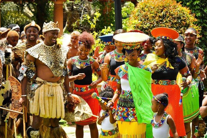 Viele Zulus feiern eine traditionelle Hochzeit, 4 Menschen im Vodergrund sind sehr bunt gekleidet