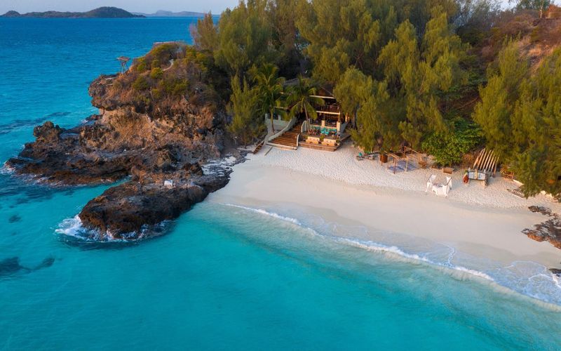 A secluded tropical beach with turquoise waters and a rustic lodge captures the serenity of African travel in May.