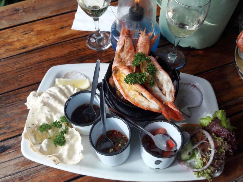 Grilled whole prawns served in a pan with dipping sauces and salad on a wooden table