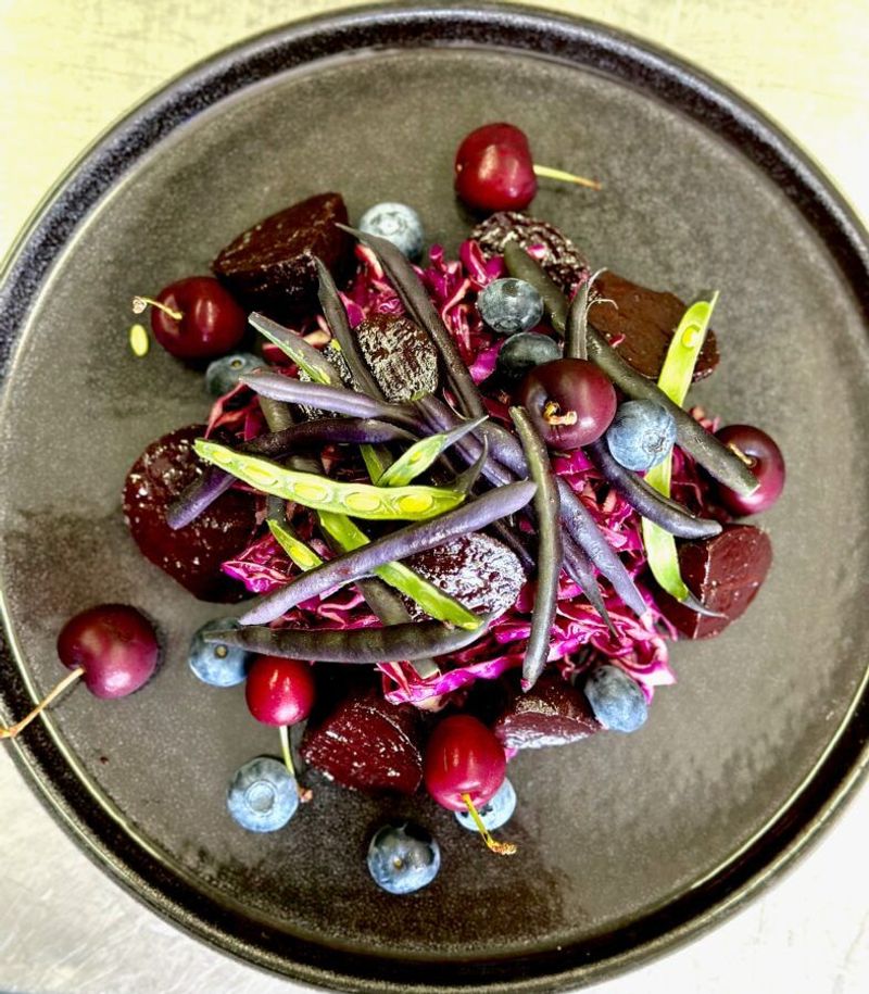 Dark plate with purple cabbage, roasted beets, purple beans, cherries, and blueberries